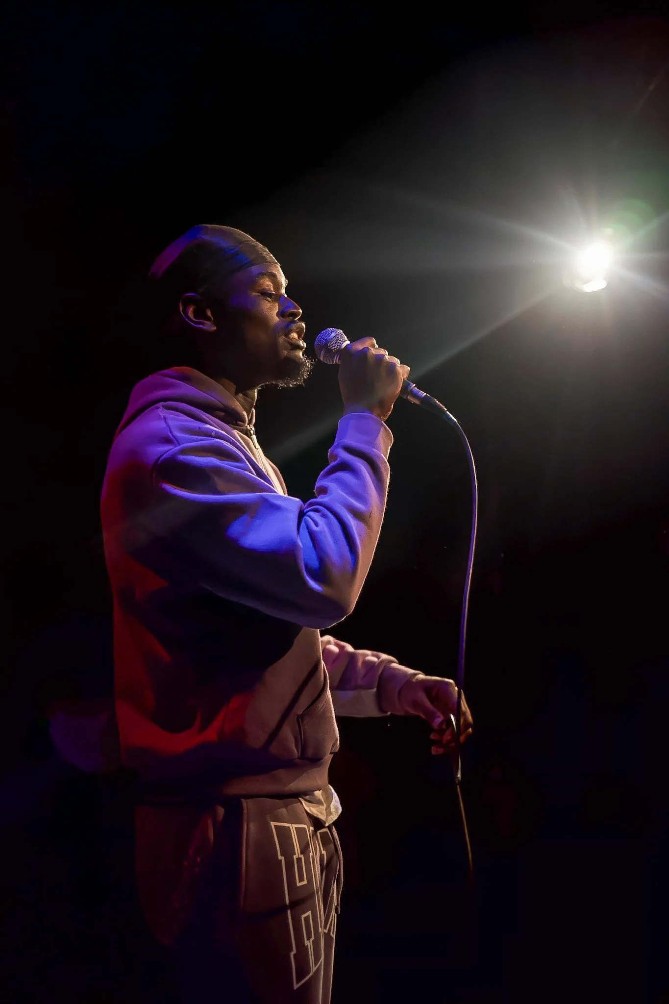 Male musician singing into a microphone on stage under a spotlight
