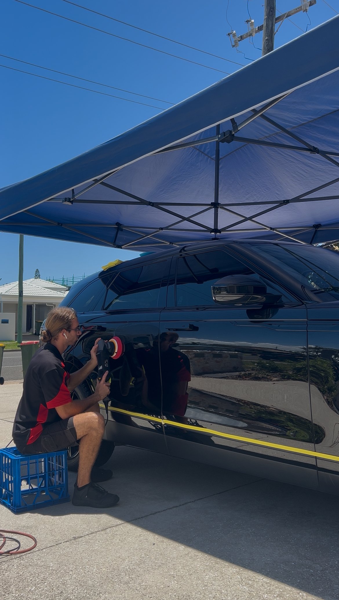 A person polishing a black car with a dual action polisher. Removing minor paint imperfections