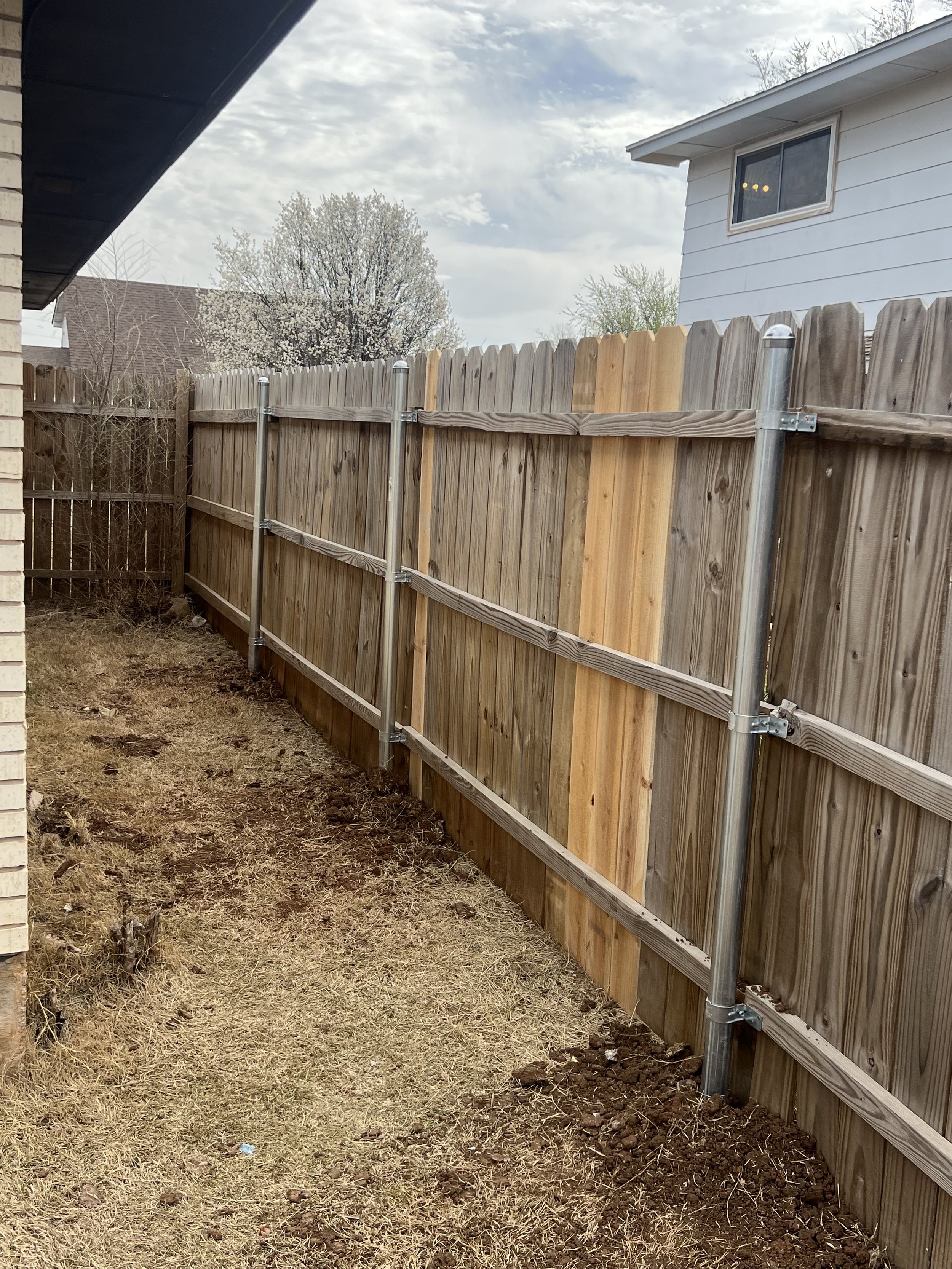 Wooden fence with metal support poles and dry grass in a backyard setting