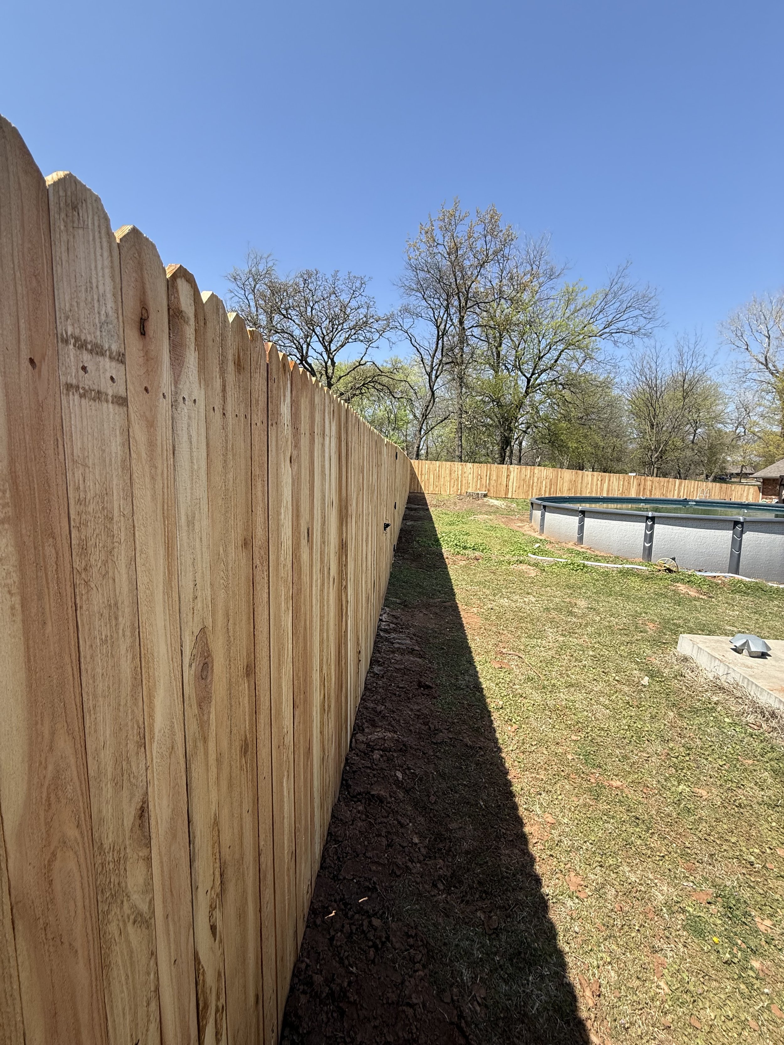 Long wooden fence in backyard with grass and trees