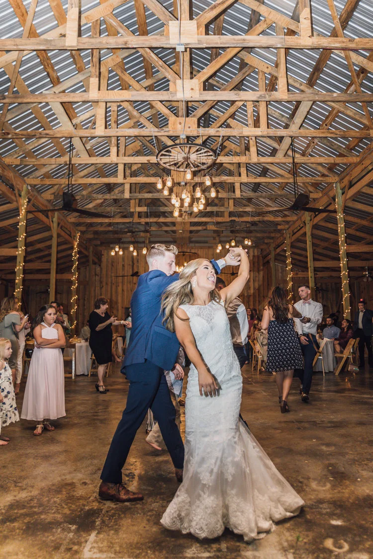 Wedding couple dancing in a barn with guests.