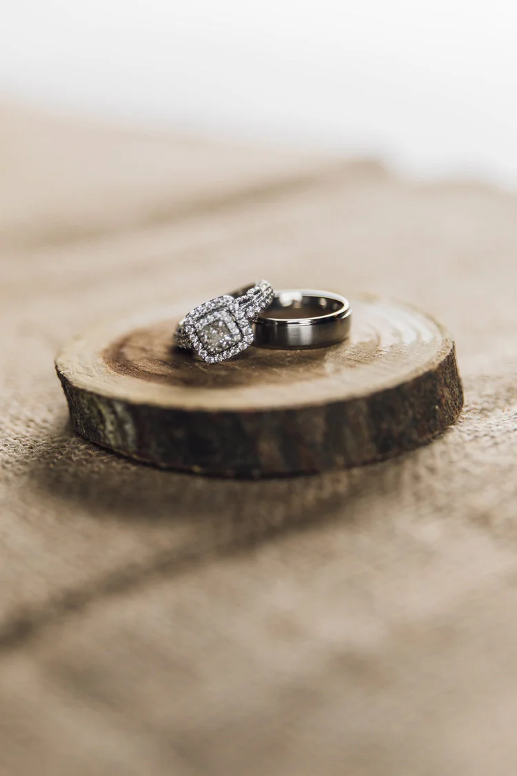 A diamond engagement ring and a plain wedding band on a wooden slice.