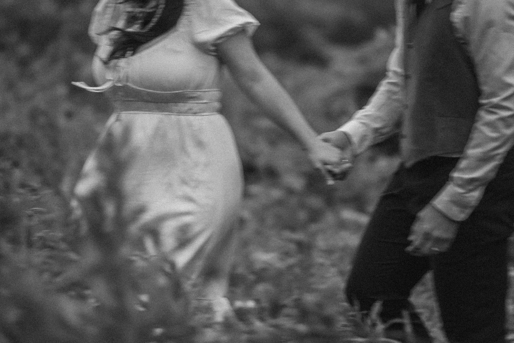 A black and white photo of a couple holding hands while walking outdoors in Glacier National Park