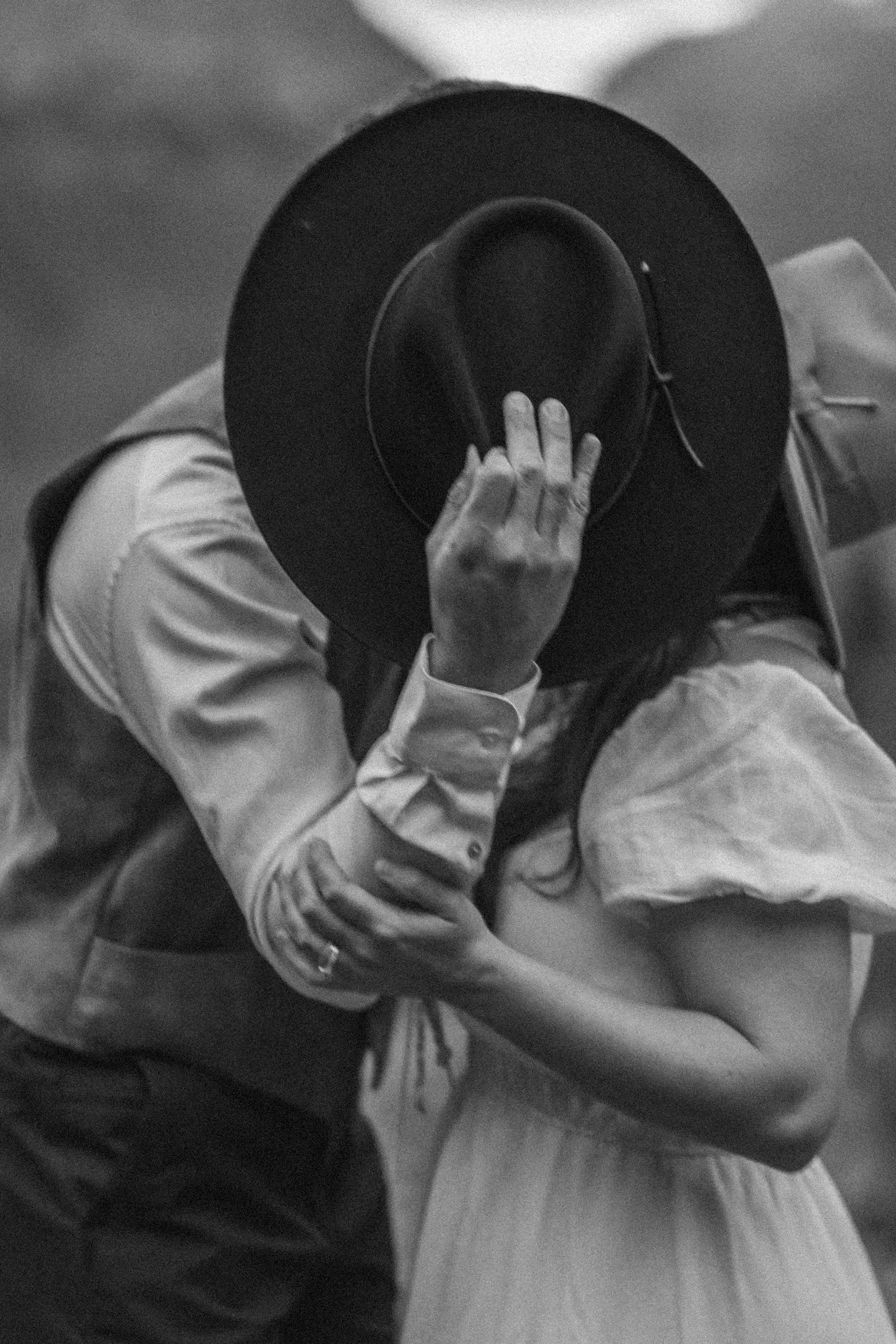 A black and white photo of a couple dancing closely, with the man wearing a hat and the woman in a dress, both holding each other in Glacier National Park