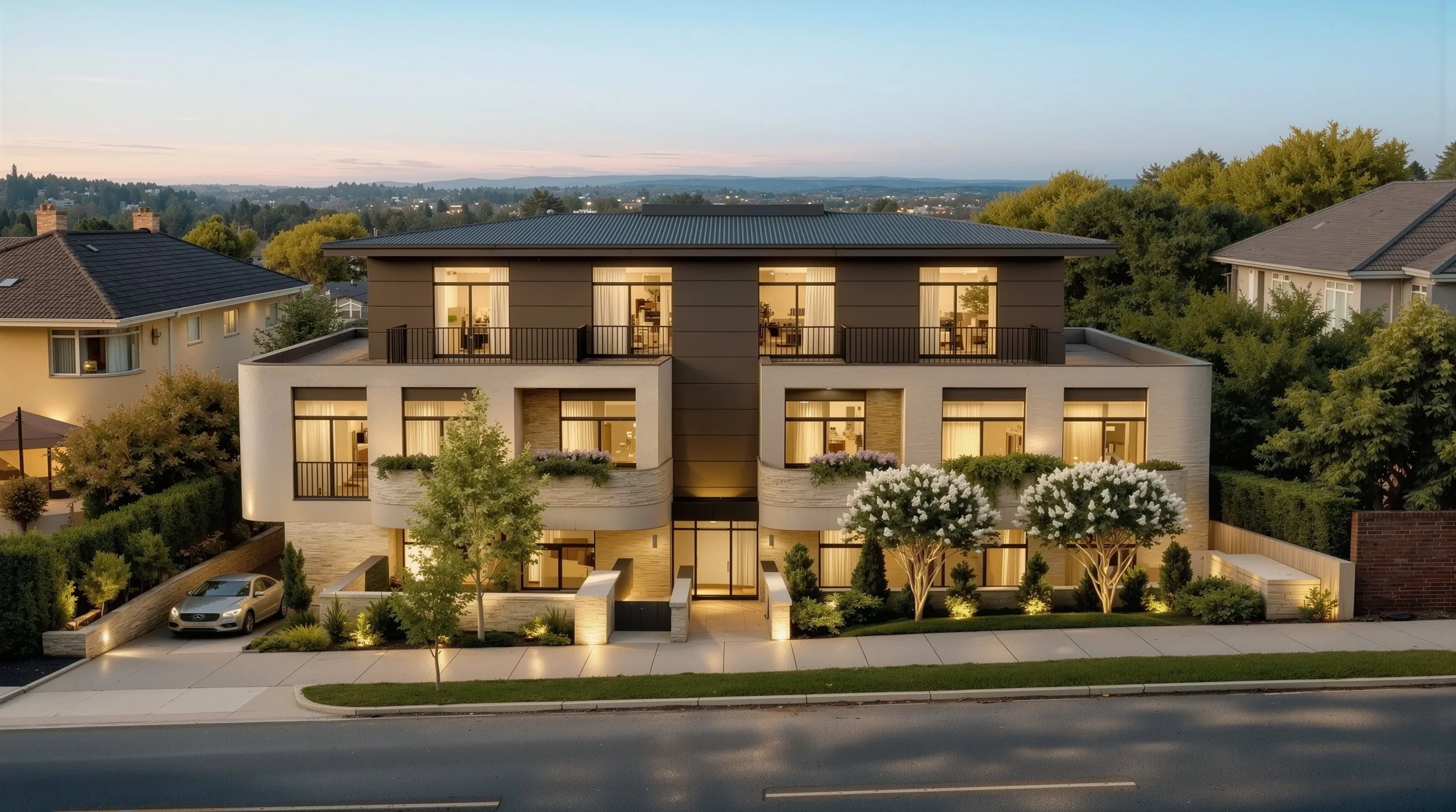 Modern multi-story apartment building at dusk with lit windows, landscaped front yard, sidewalk, and neighboring houses.