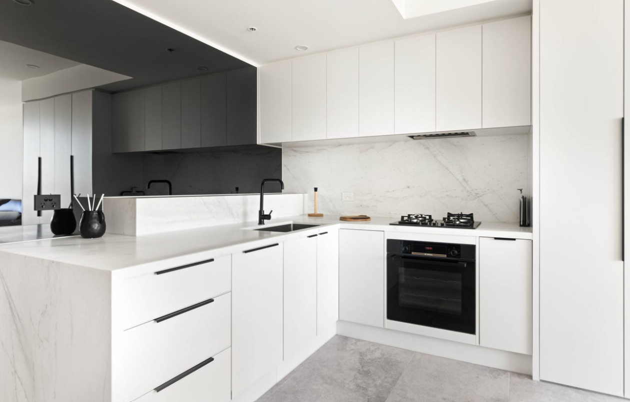 Modern kitchen with white cabinets, a white marble countertop, black faucet, built-in black oven, gas stove, and minimal decor.