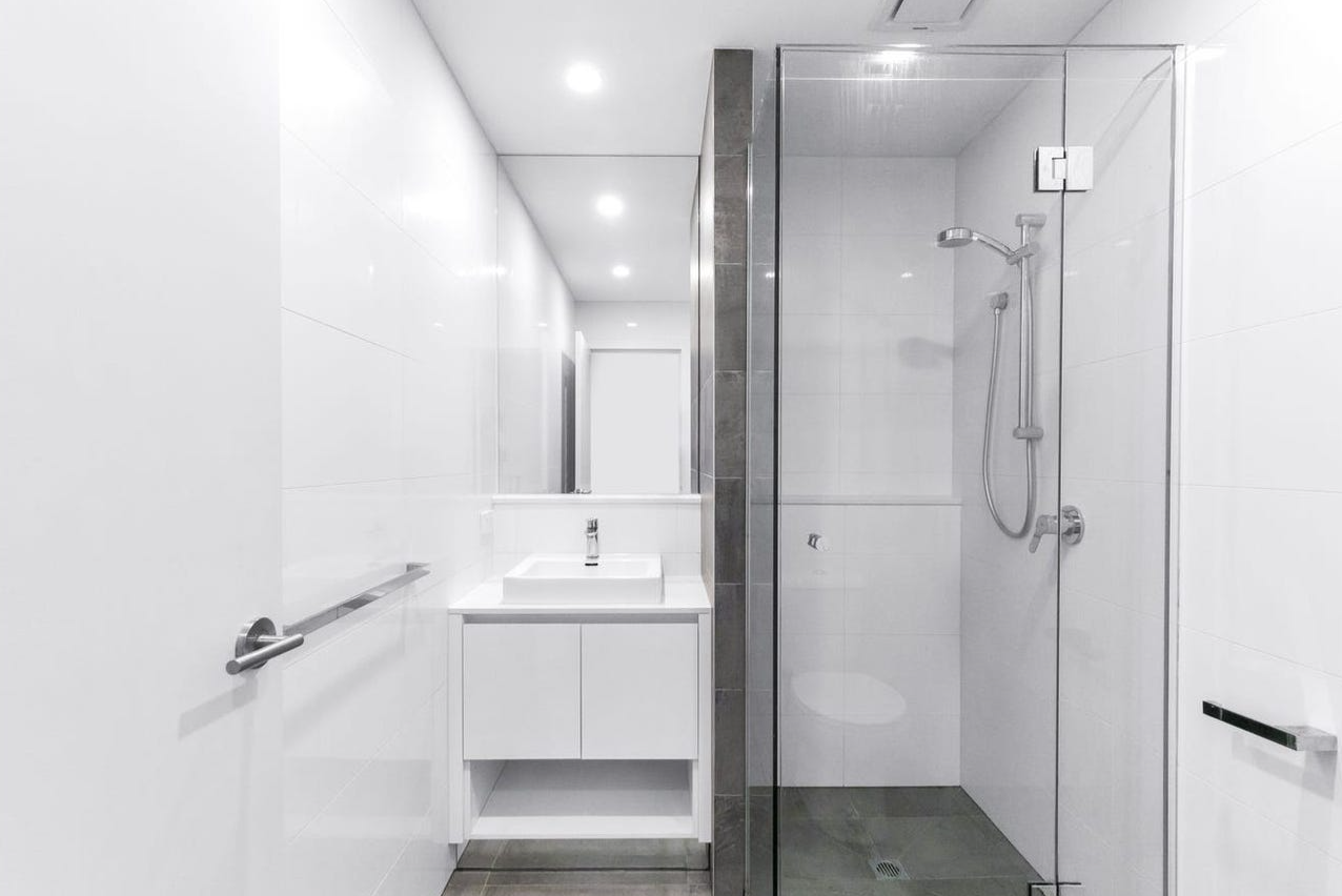 Modern, minimalist bathroom with a white sink, mirror, and a glass-enclosed shower with a rain showerhead.