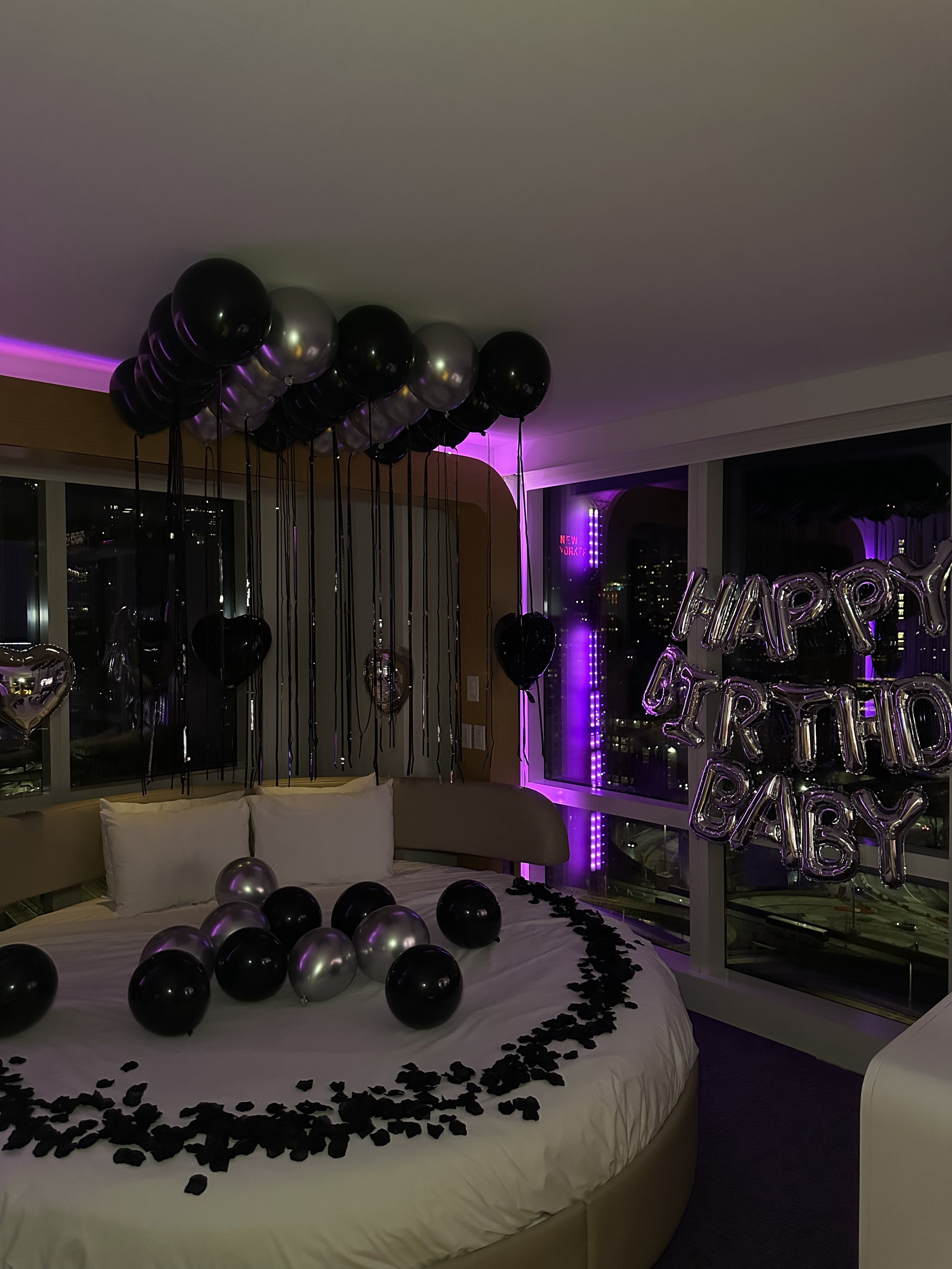 Hotel room decorated with black and silver balloons, 'Happy Birthday Baby' banner, and black rose petals