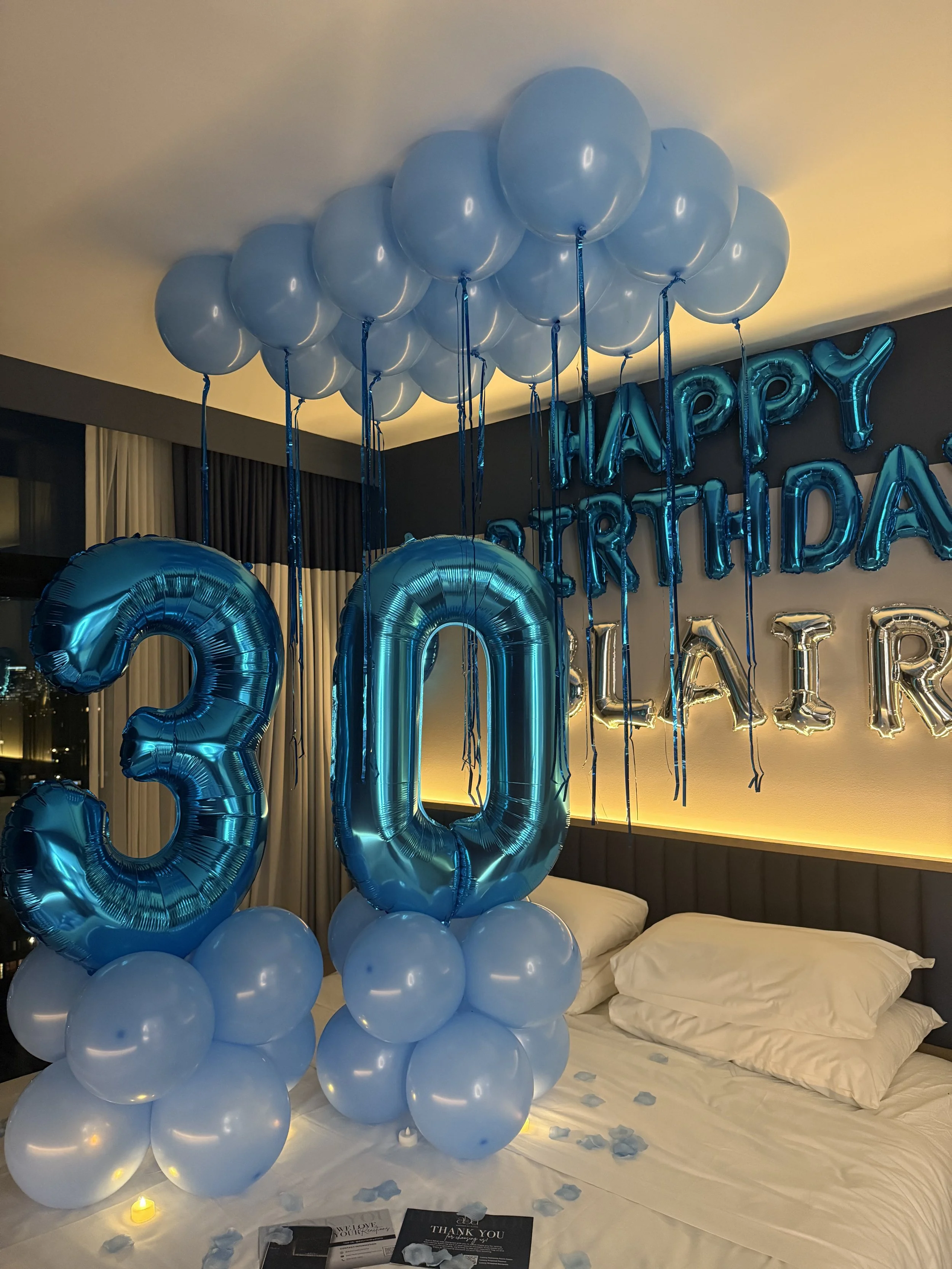 Hotel room decorated with blue and silver balloons, 'Happy Birthday Blair' banner, large blue number balloons