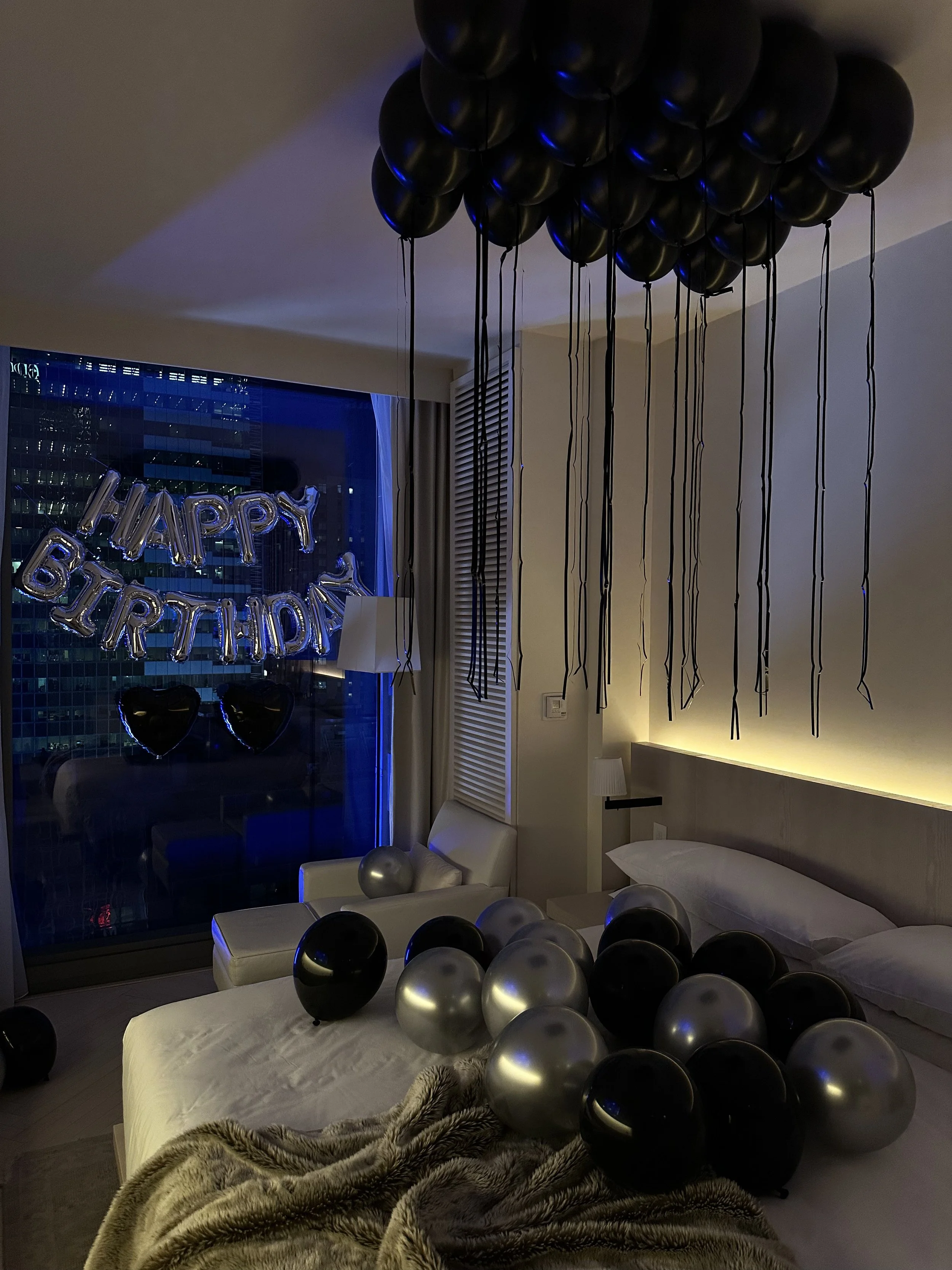 Hotel room decorated with black and silver balloons, 'Happy Birthday' banner, and heart balloons
