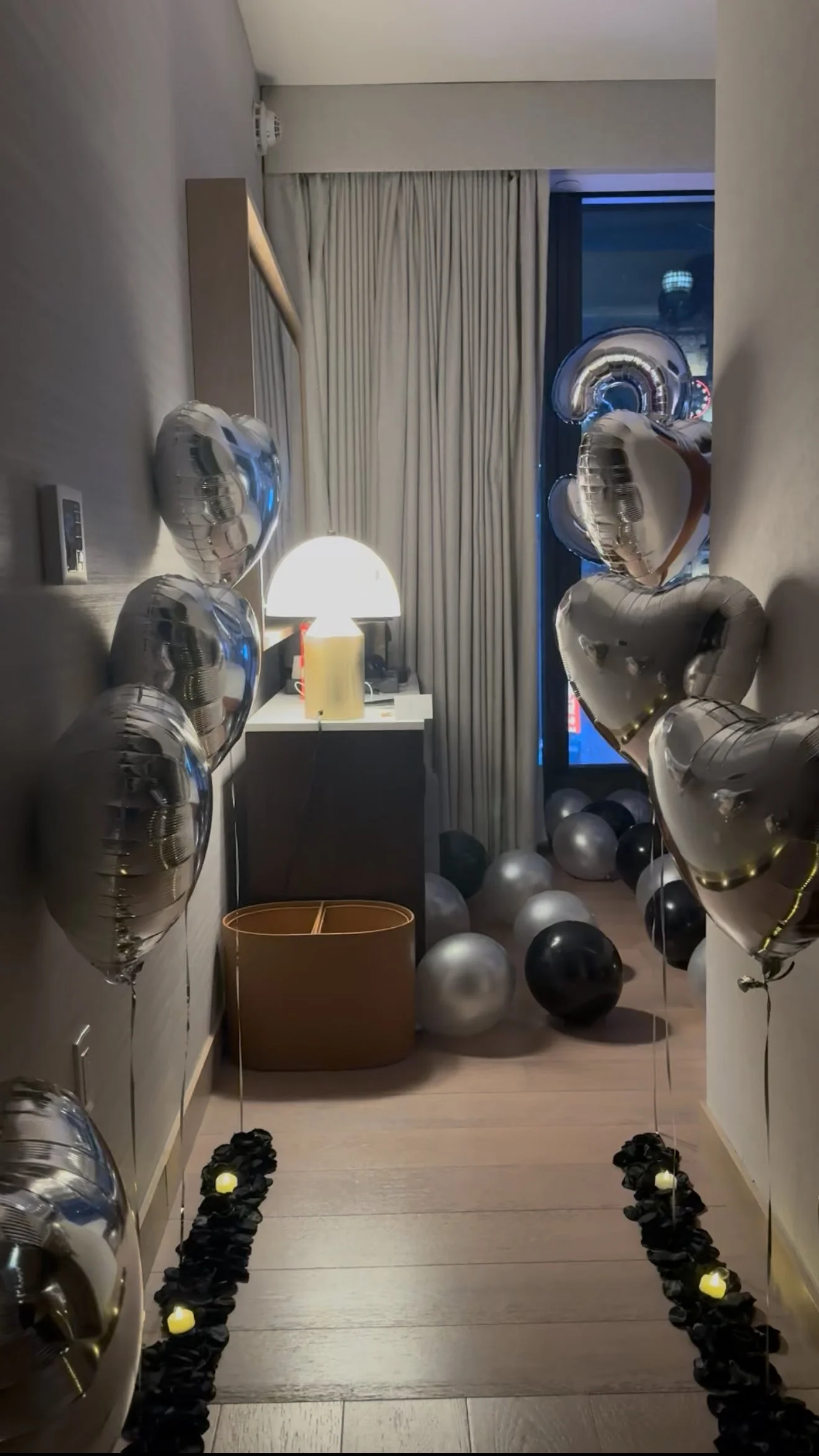 Hotel room decorated with black and silver balloons, large silver number balloons, and black rose petals