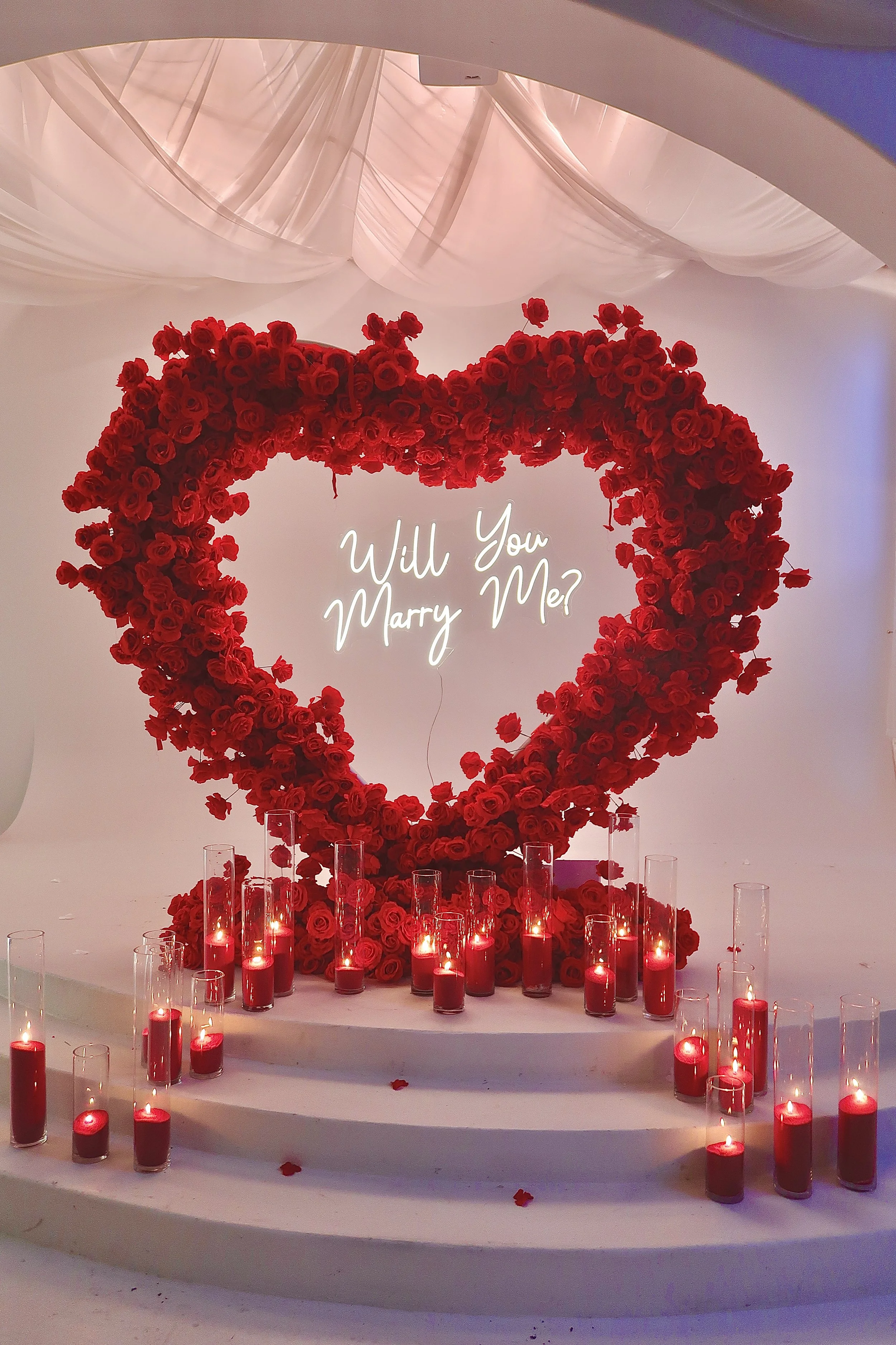 Luxury proposal setup with 8 ft red rose heart arch, red sand wax candles and neon 'Marry Me' signin NYC