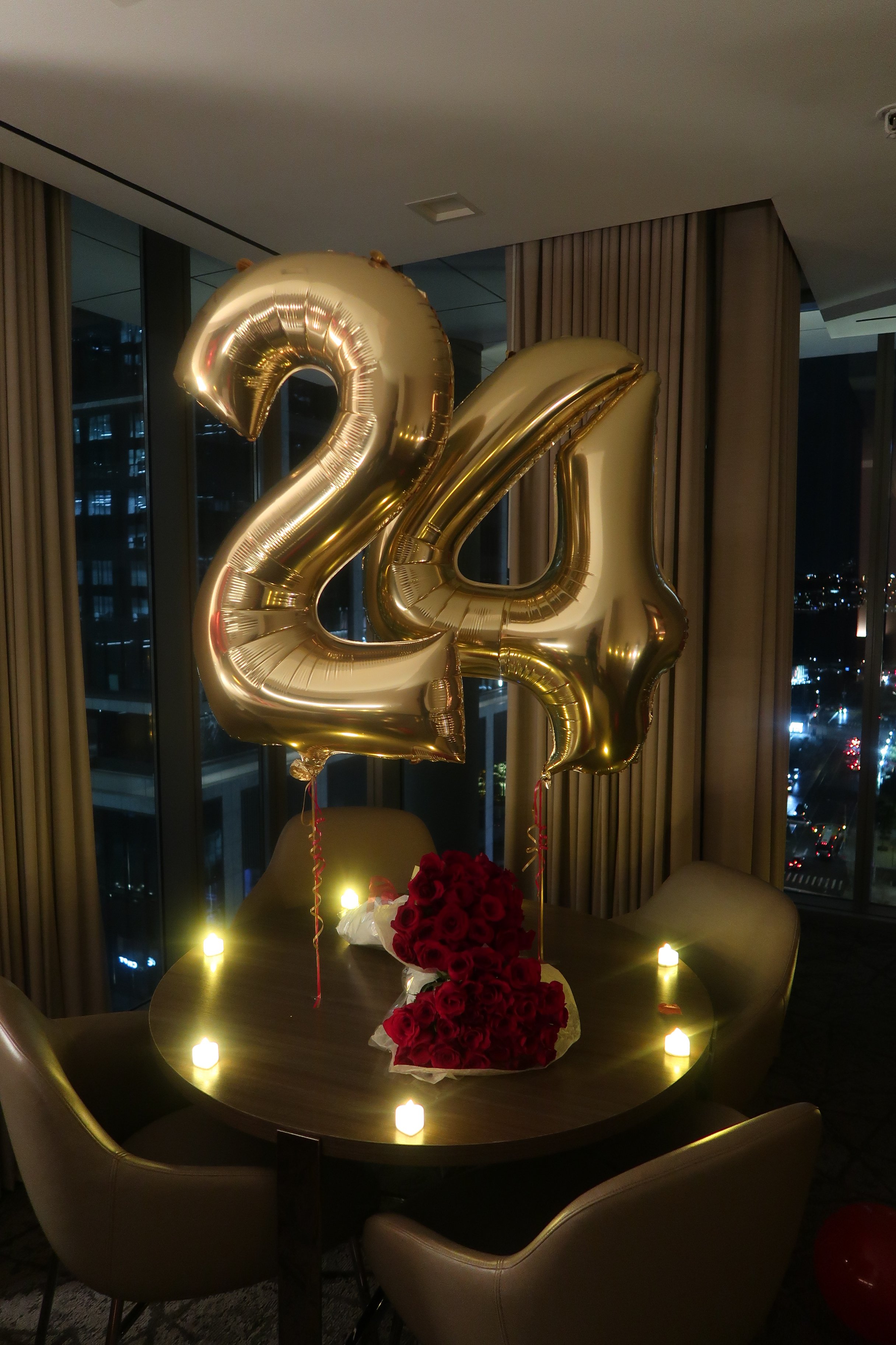 Hotel room decorated with large gold number balloons, 2 dozen red rose bouquets and heart shaped LED candles