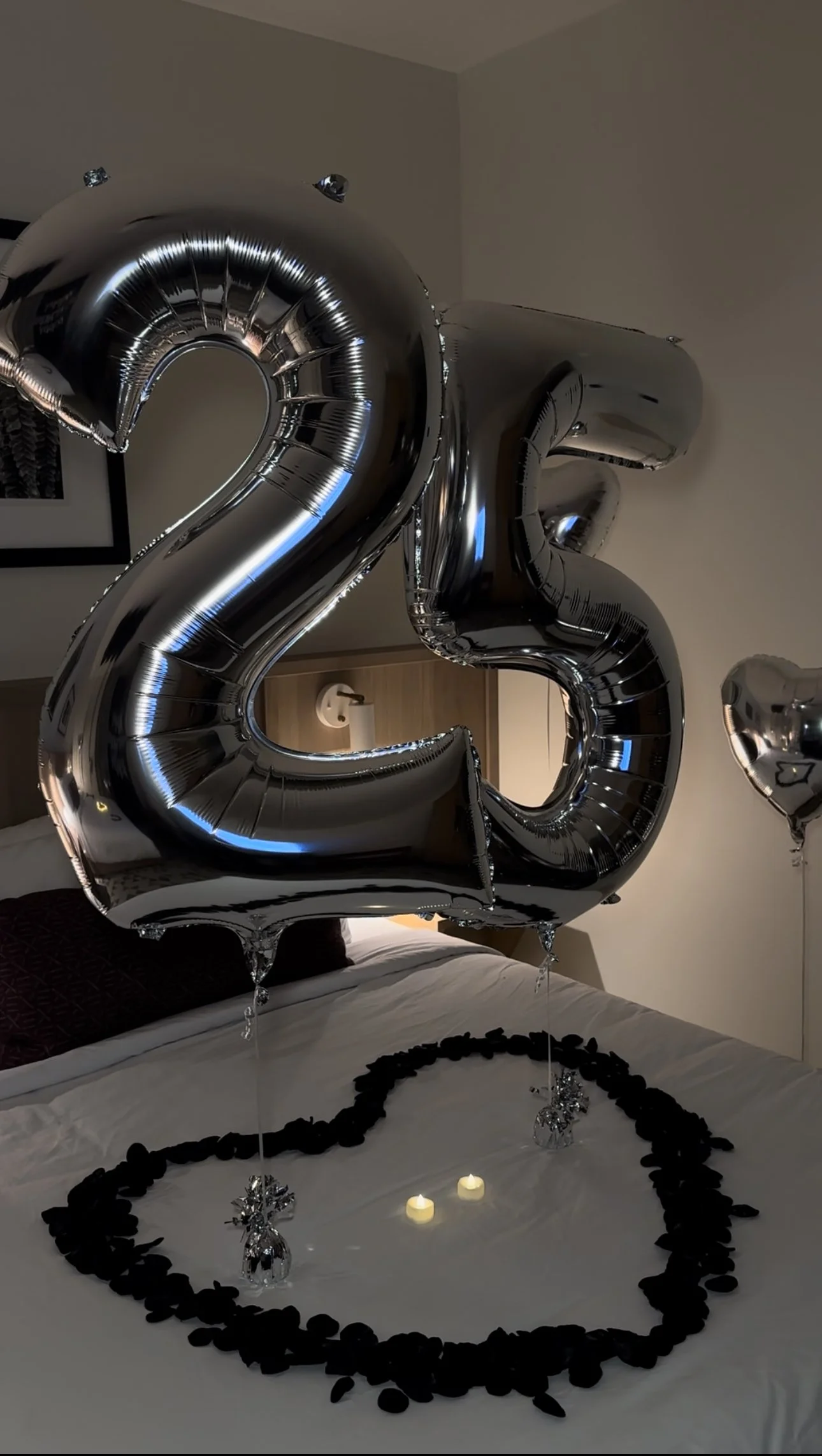 Hotel room decorated with large silver number balloons, black rose petals and LED candles