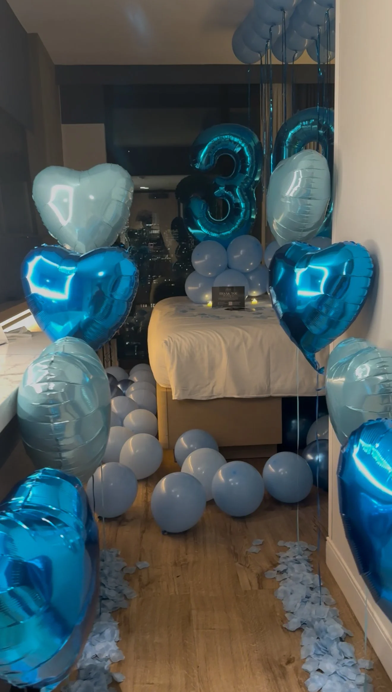 Hotel room decorated with blue and silver balloons ,  large blue number balloons and blue rose petals