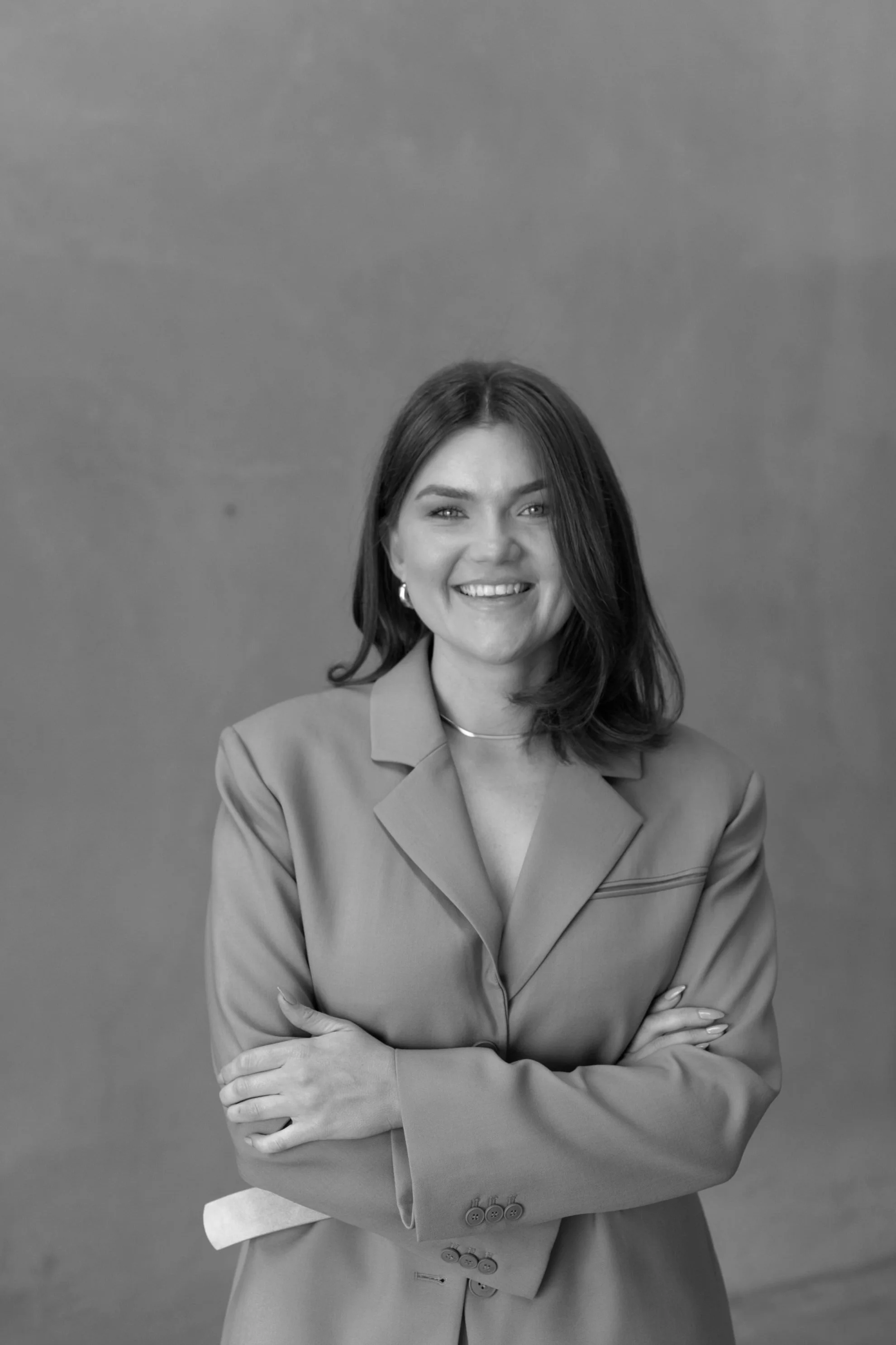 Black and white portrait of a woman smiling with arms crossed, wearing a blazer.