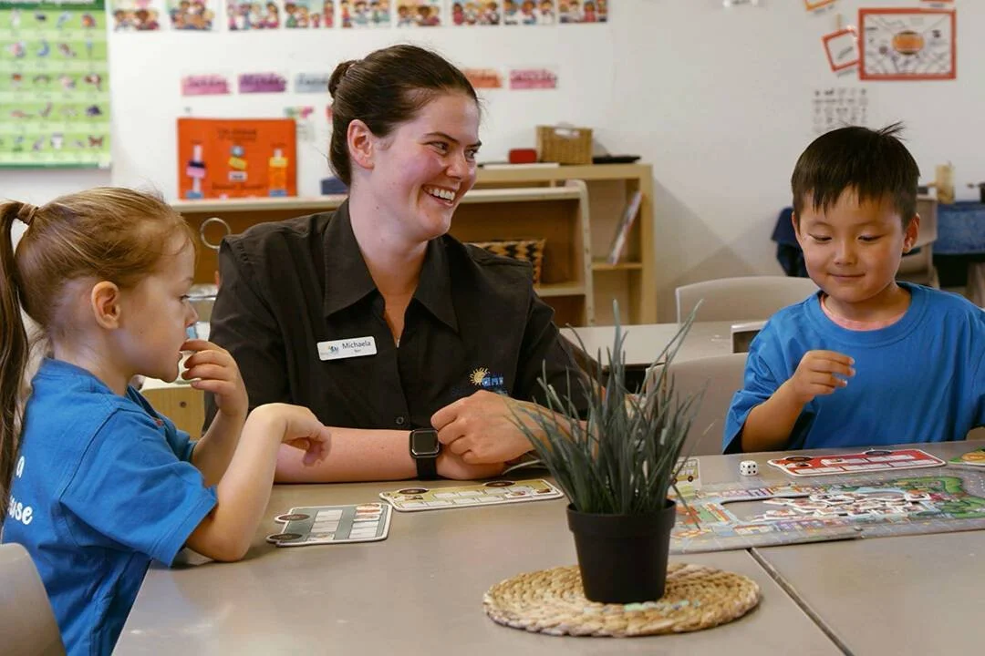 A teacher and two children playing a board game in a classroom.