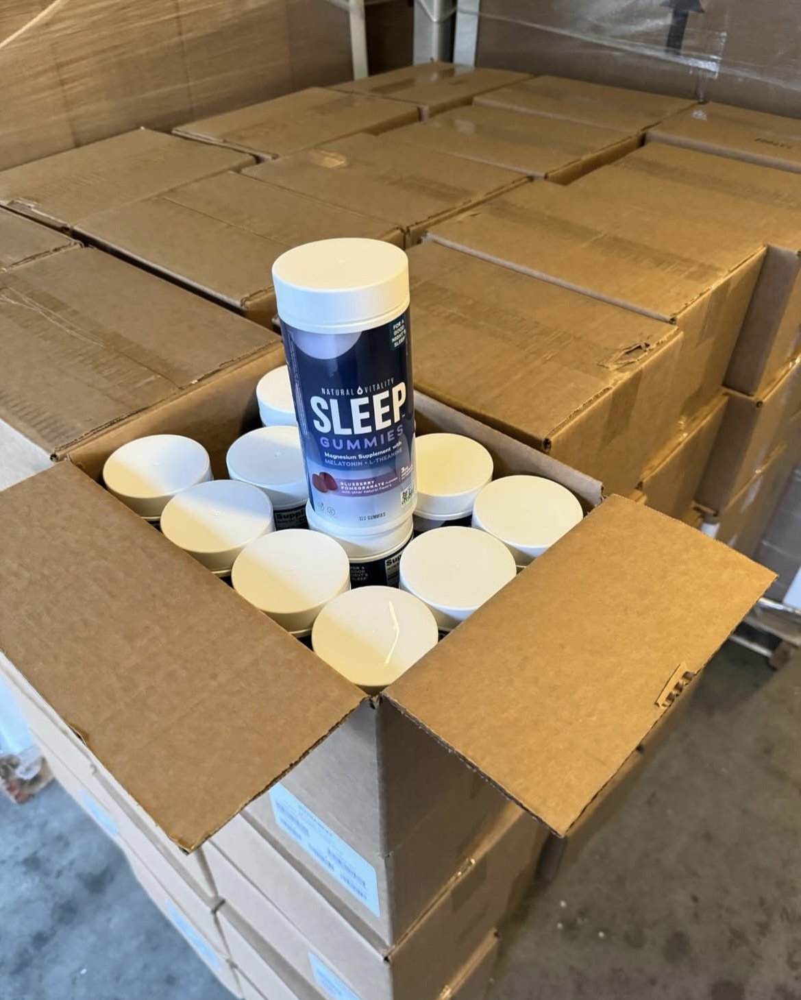 Box of sleep gummies with multiple bottles, stacked on top of more boxes in a storage area.