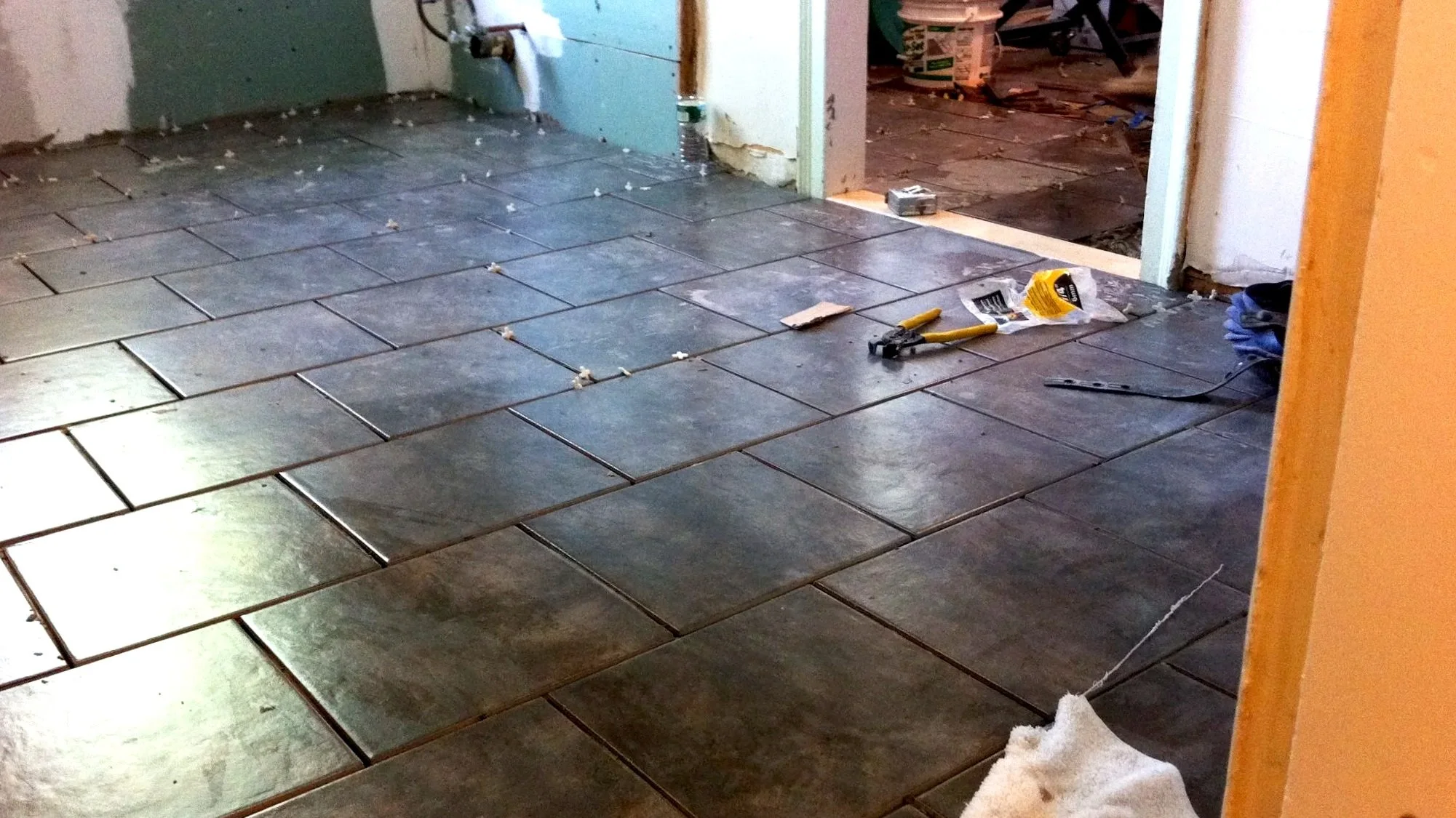 Room under renovation with installed dark floor tiles, scattered tools, and construction materials.