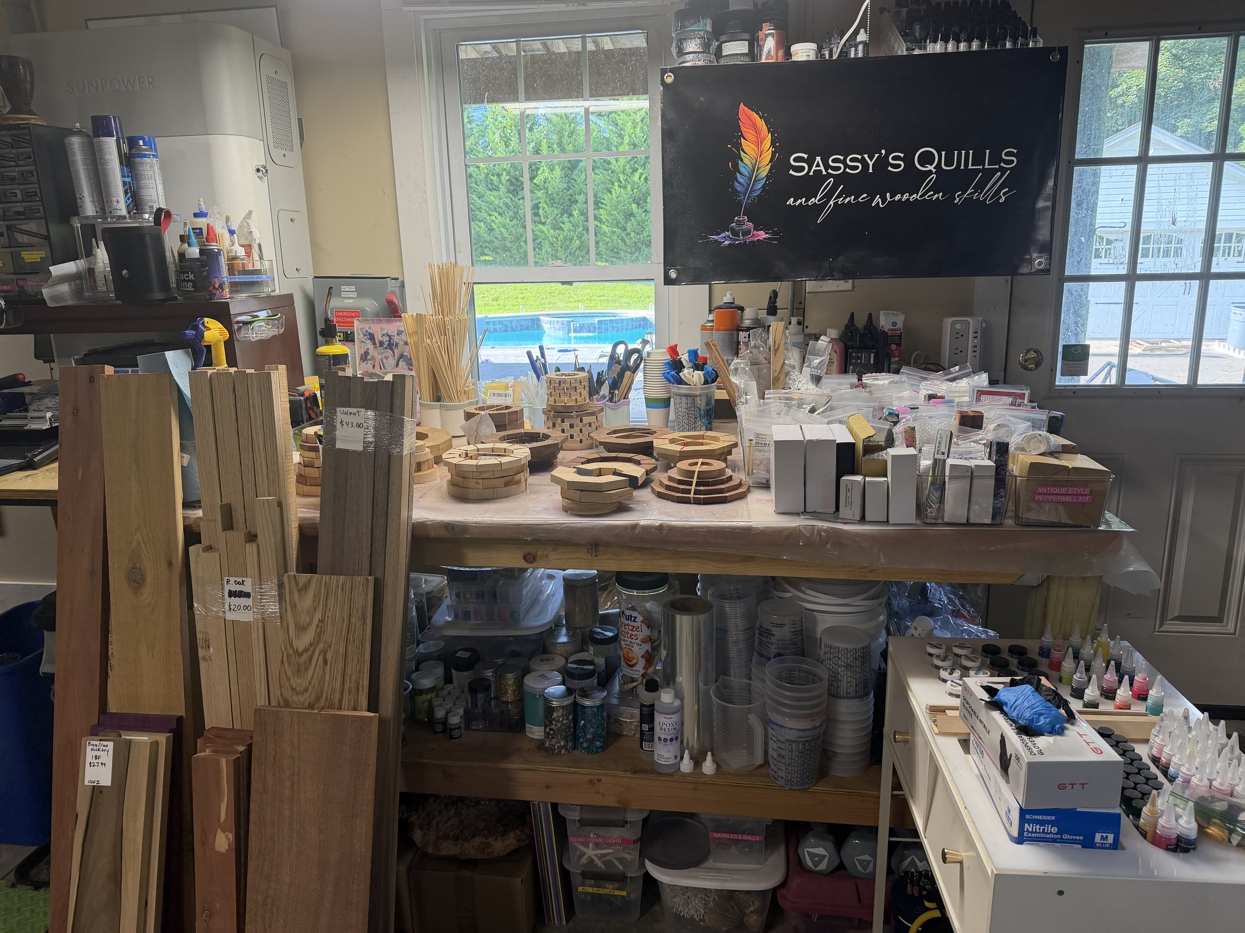 Workshop with various woodworking and art supplies, including wooden pieces, paints, brushes, and tools, with a window showing a green outdoor landscape.