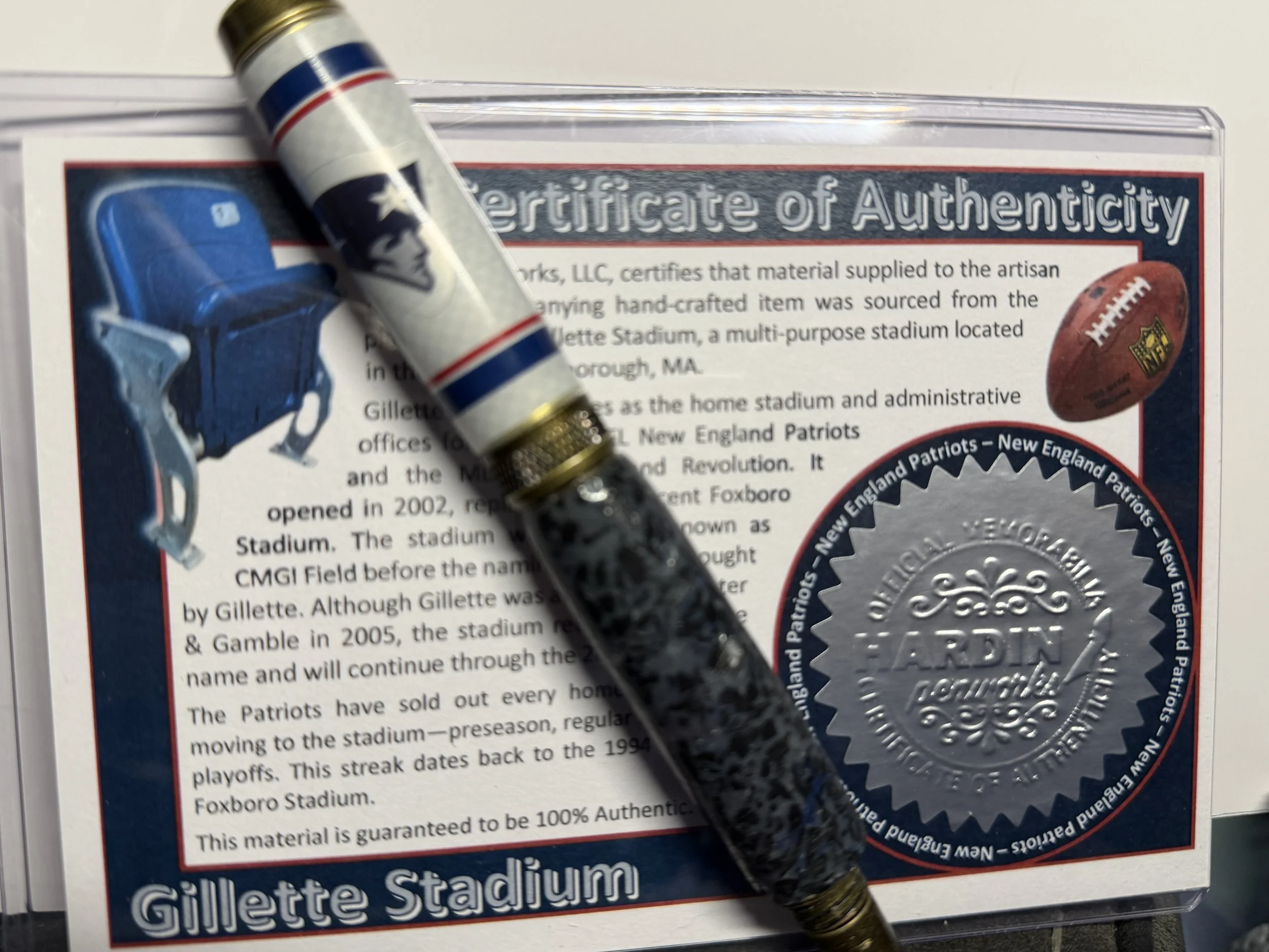Close-up of a certificate of authenticity with a small football pin and a marker placed on top of it, featuring text about Gillette Stadium and the New England Patriots.