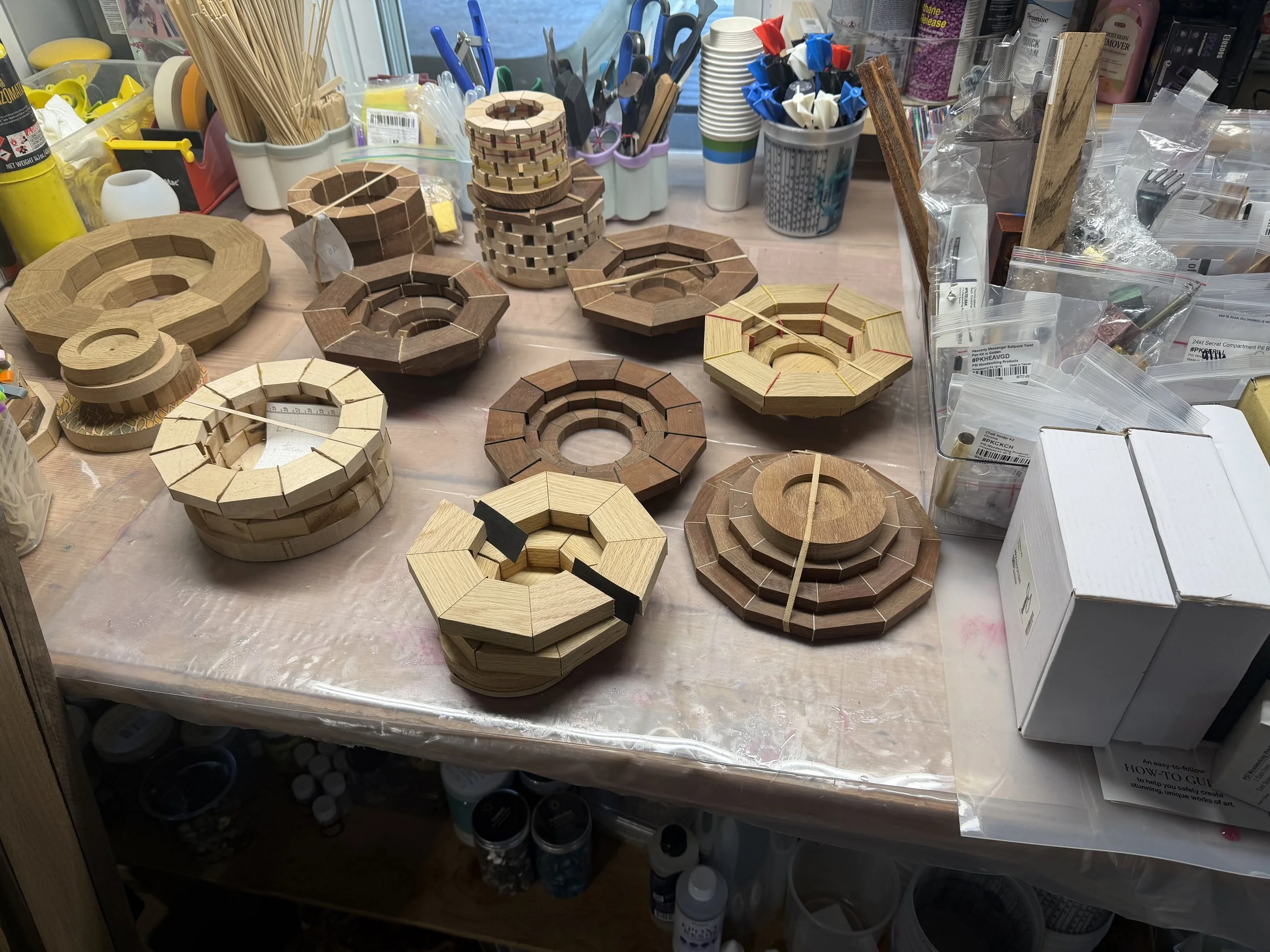 Workspace with various wooden geometric designs, crafting supplies, and tools on a cluttered table.