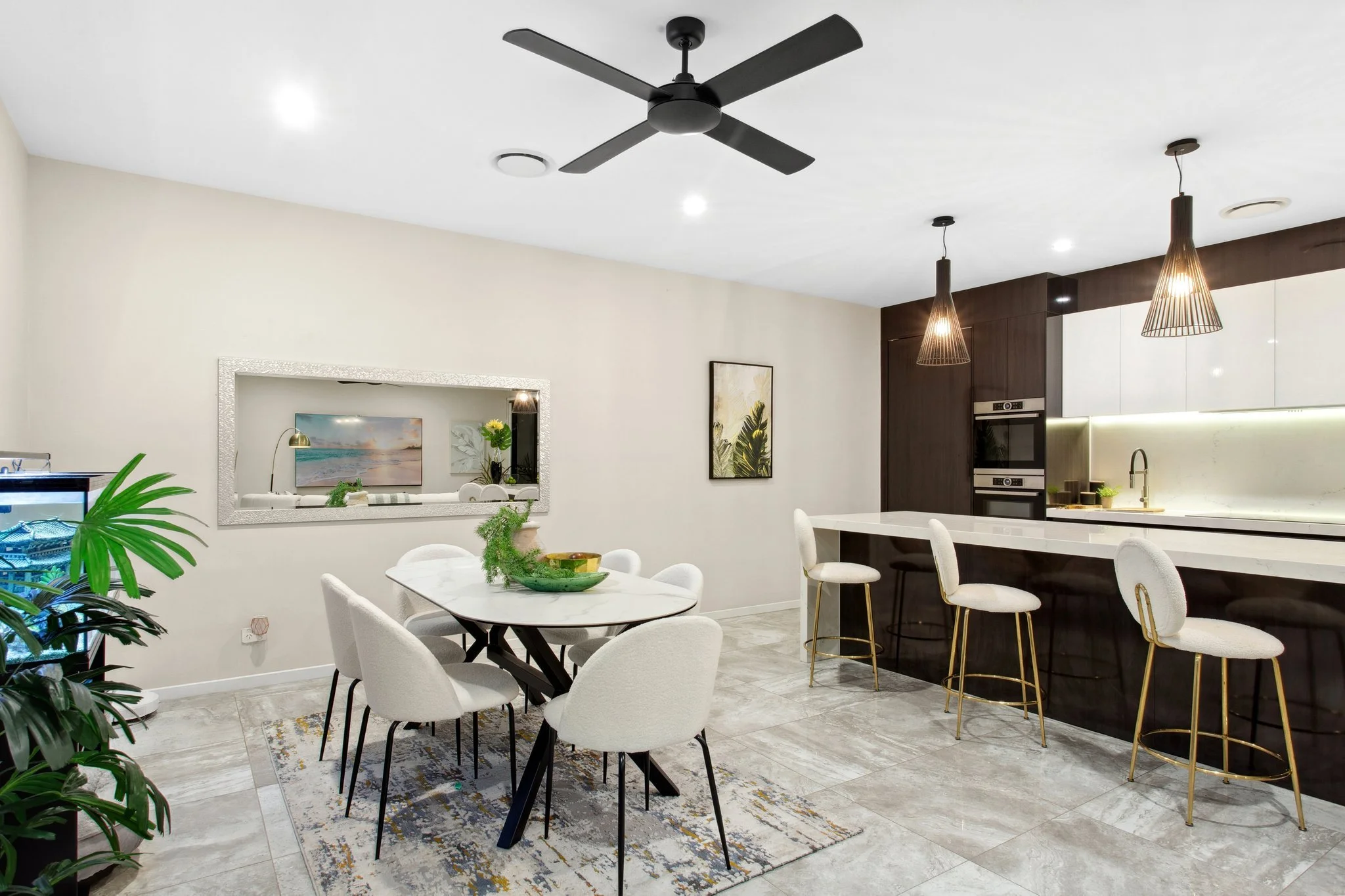 Modern kitchen and dining area with a white marble table and six chairs, a large island with three bar stools, pendant lights, a ceiling fan.
