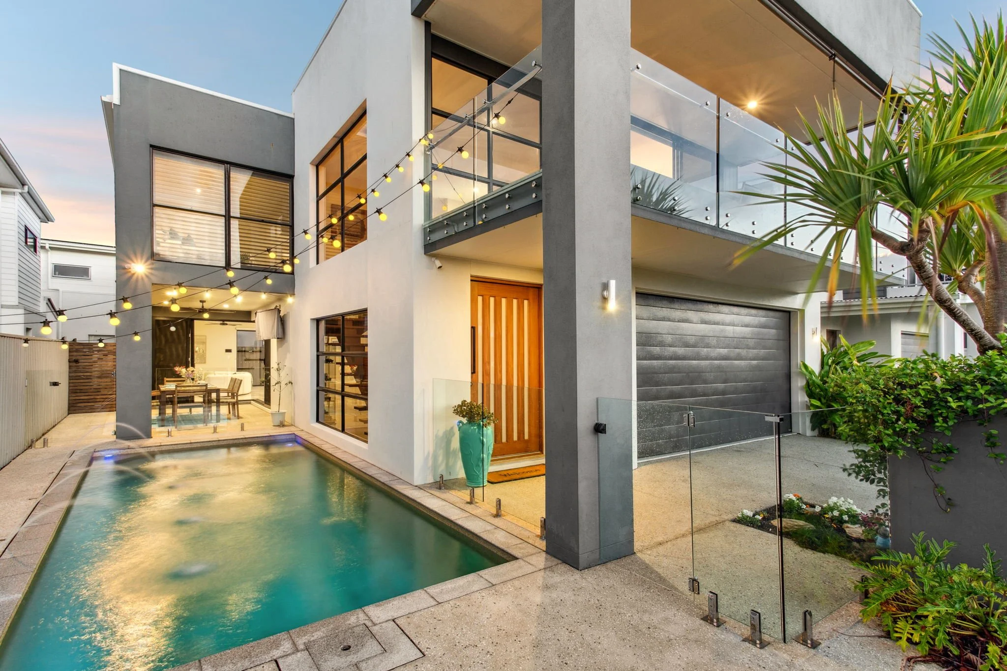 Modern house exterior with pool, glass railing, and outdoor lights.