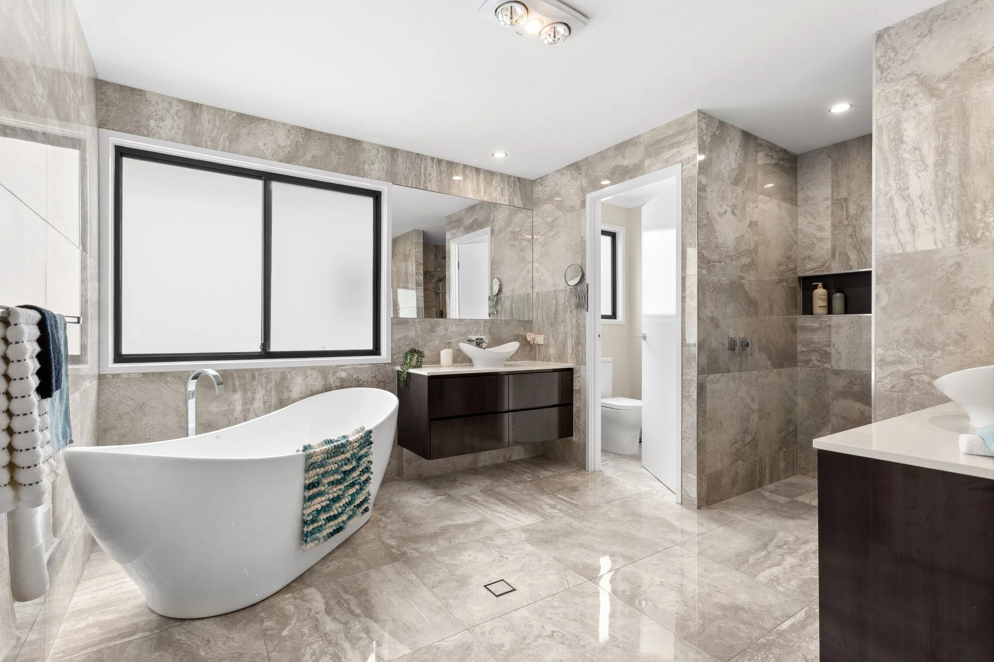 Modern bathroom with freestanding bathtub, large window, and polished travertine tiles.