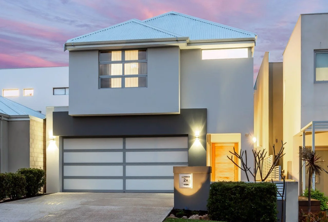Modern two-story house with gray exterior, large windows, and double garage, illuminated by outdoor lights.