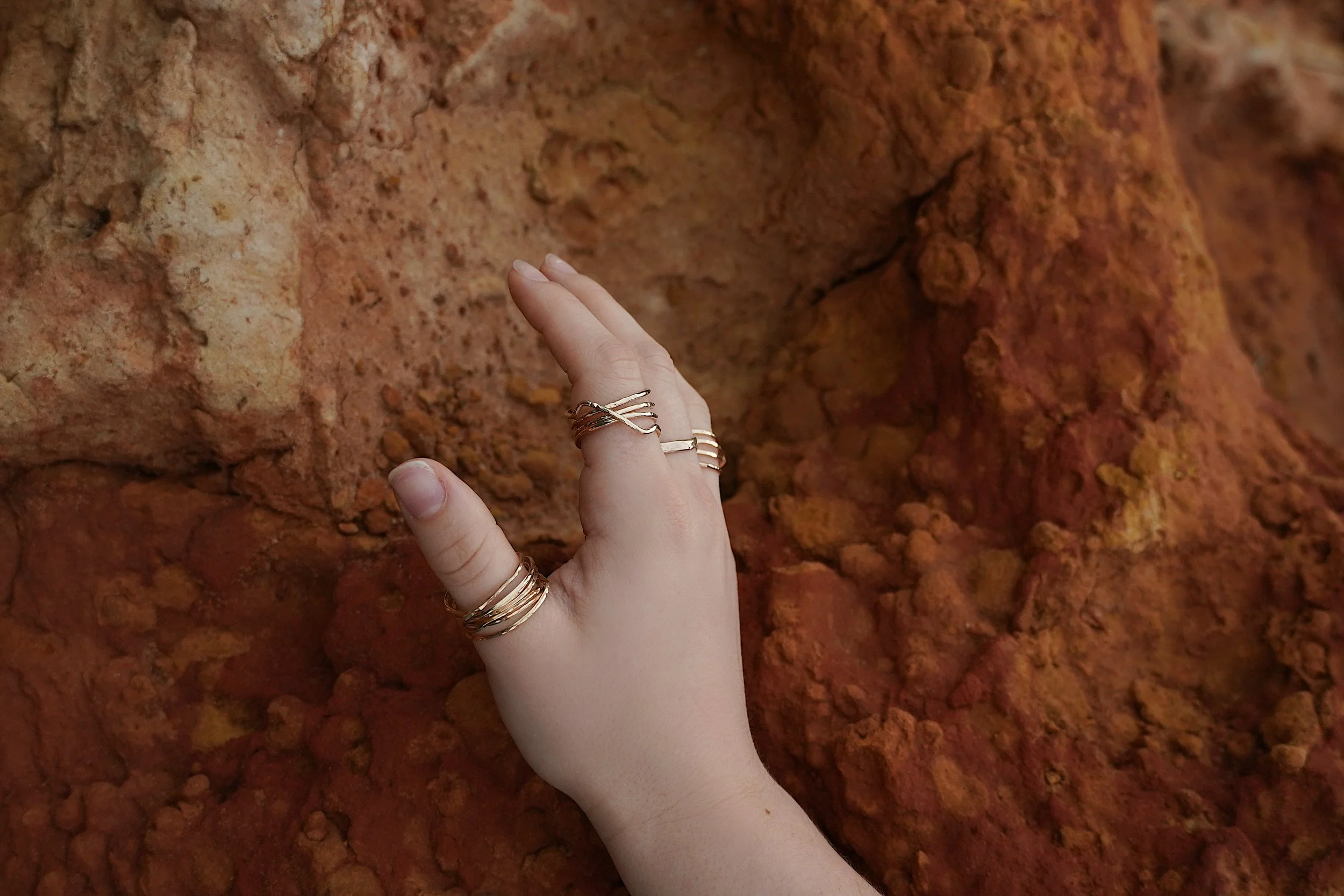 A person's left hand with multiple rings touching red textured rocks.