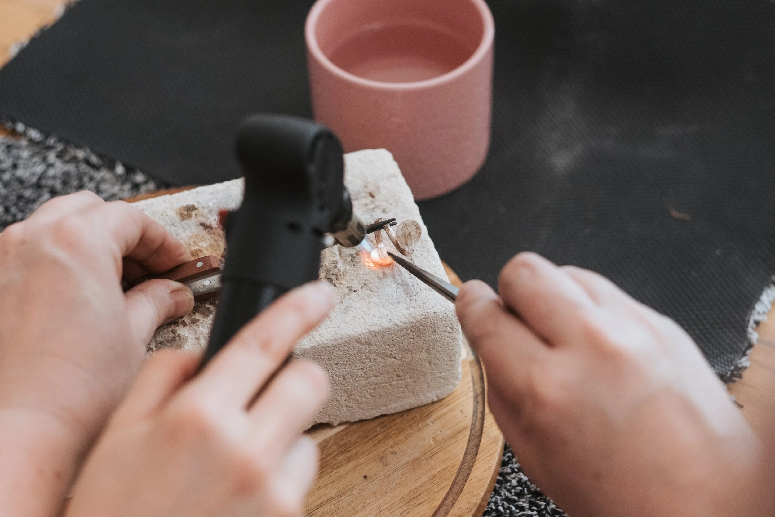 Person using a laser welder to fuse glass pieces on a stone surface, with a pink ceramic cup in the background.