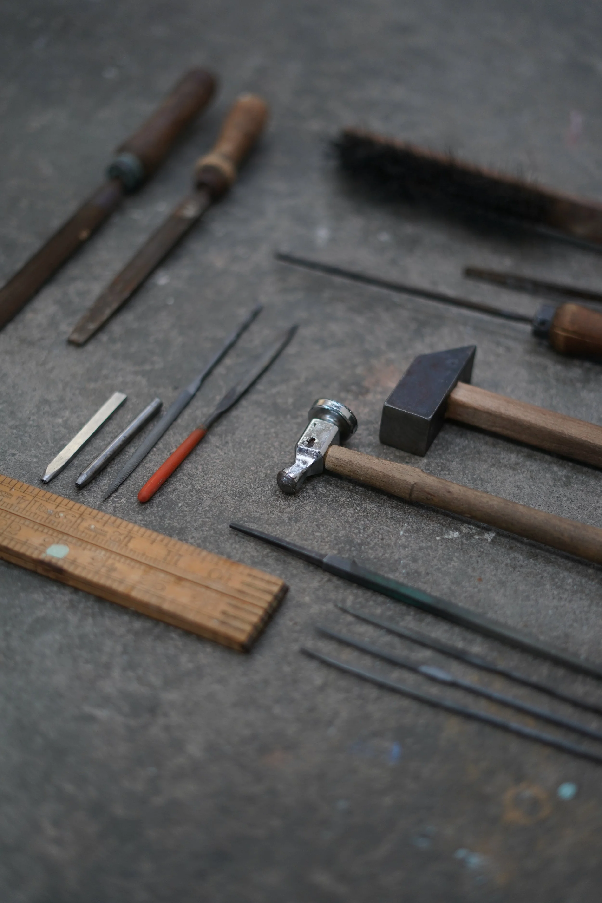 Various hand tools including chisels, a hammer, chiseling tools, a ruler, and a file spread out on a workbench.