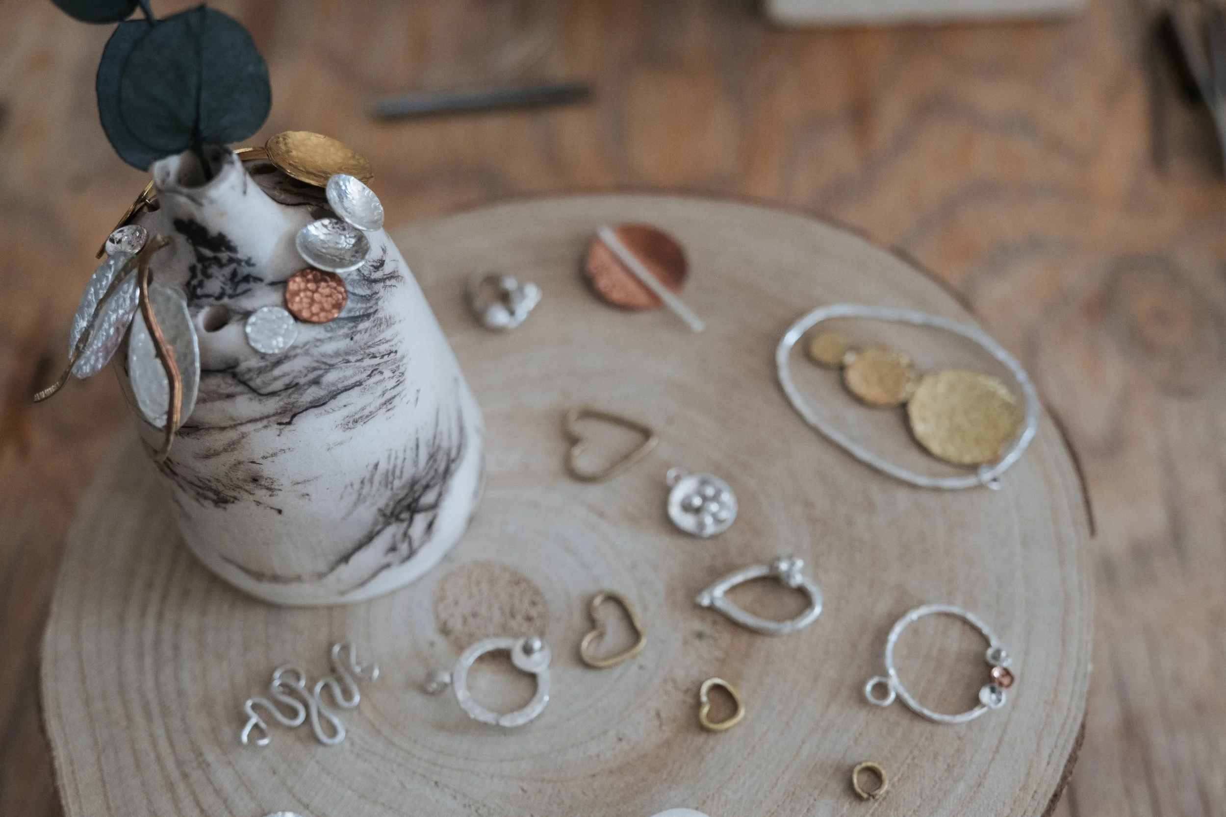 A marble-patterned vase with green leaves, surrounded by various jewelry pieces including rings, earrings, and necklaces, placed on a wooden surface.