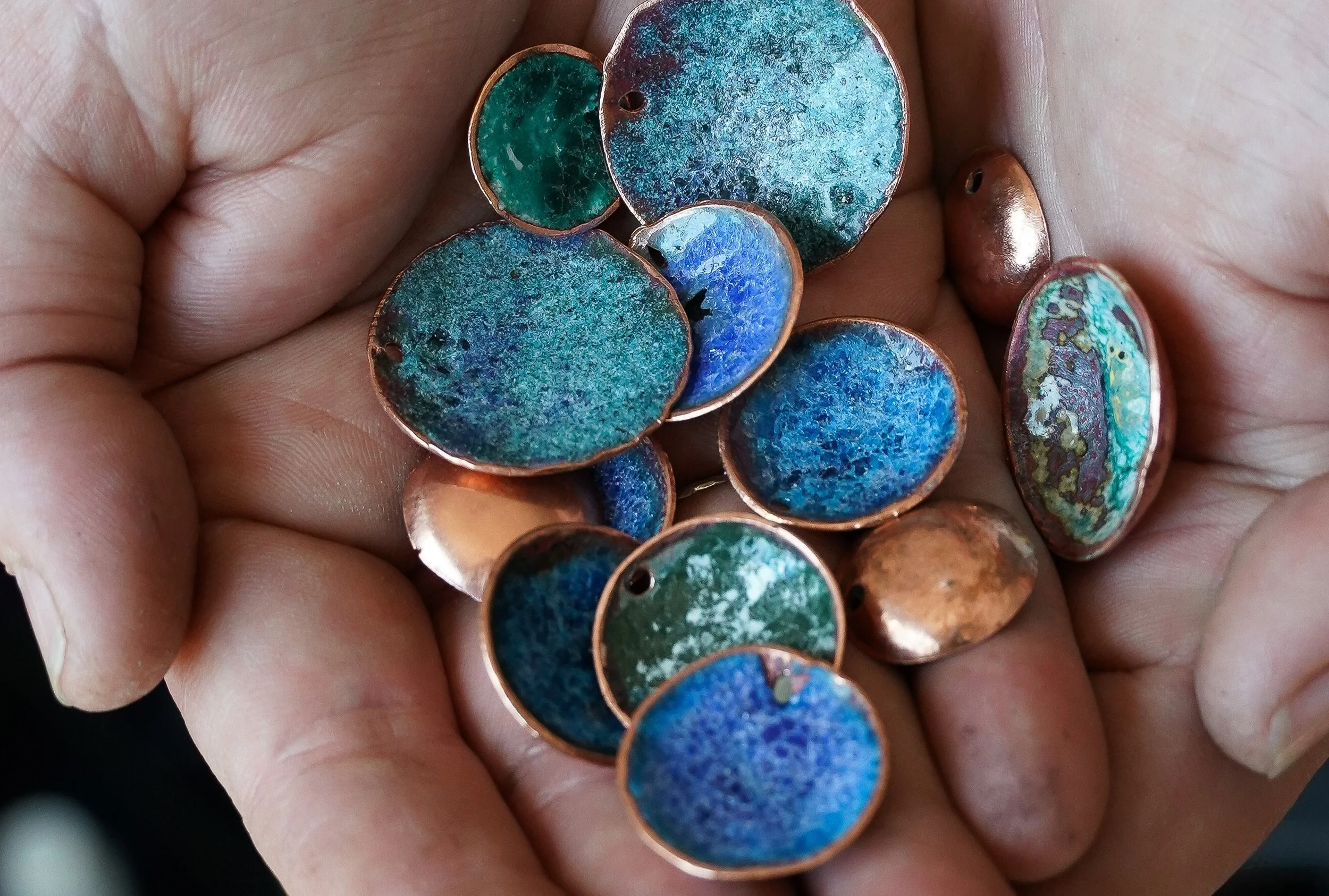 A handful of assorted, round, copper-colored jewelry pieces with blue, green, and iridescent colored inlays.