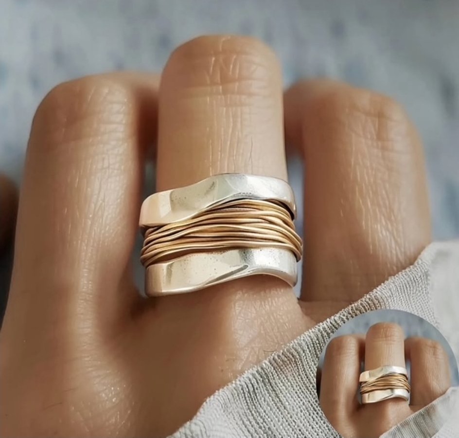 The image shows a close up of a hand with a chunky silver ring wrapped in a gold coloured metal.