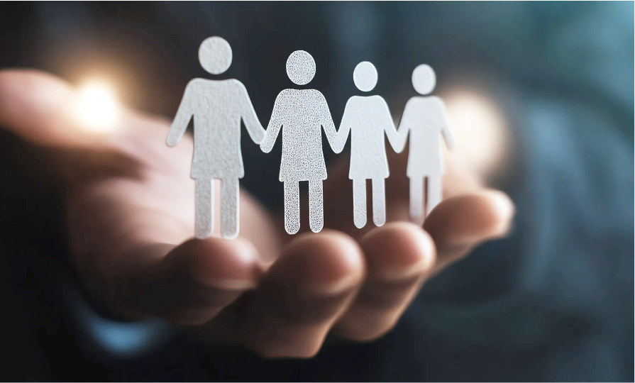 A person's hand holding four paper cutouts of women holding hands, symbolizing community or unity.