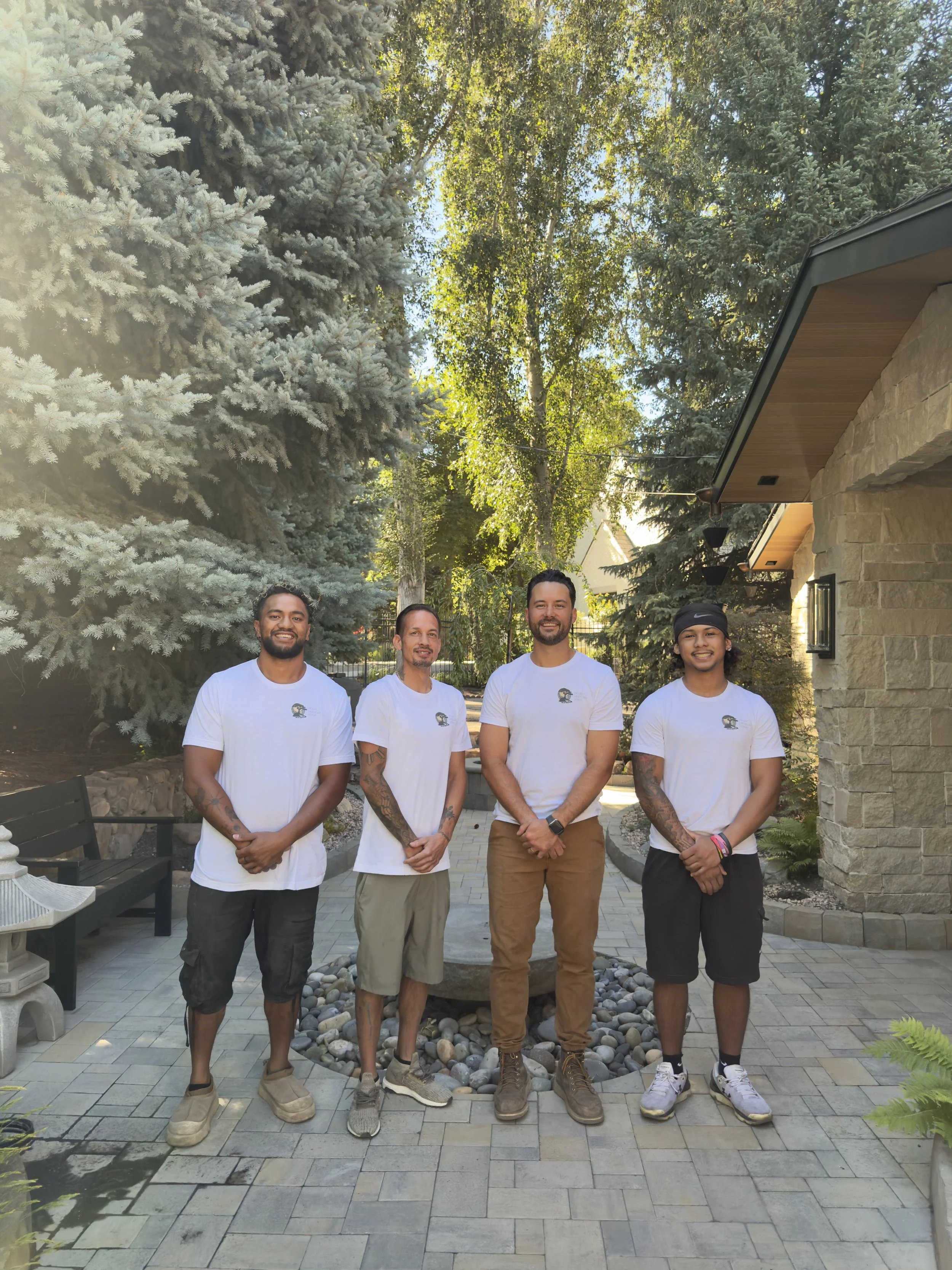 Four men in white shirts standing together on a paved garden walkway.