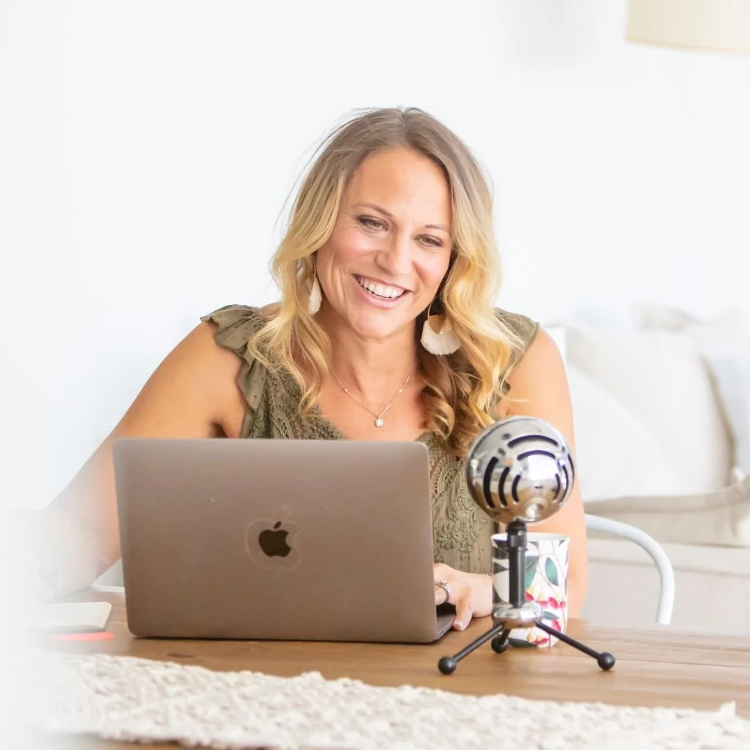 Woman smiling while using a laptop, with a microphone on the table.