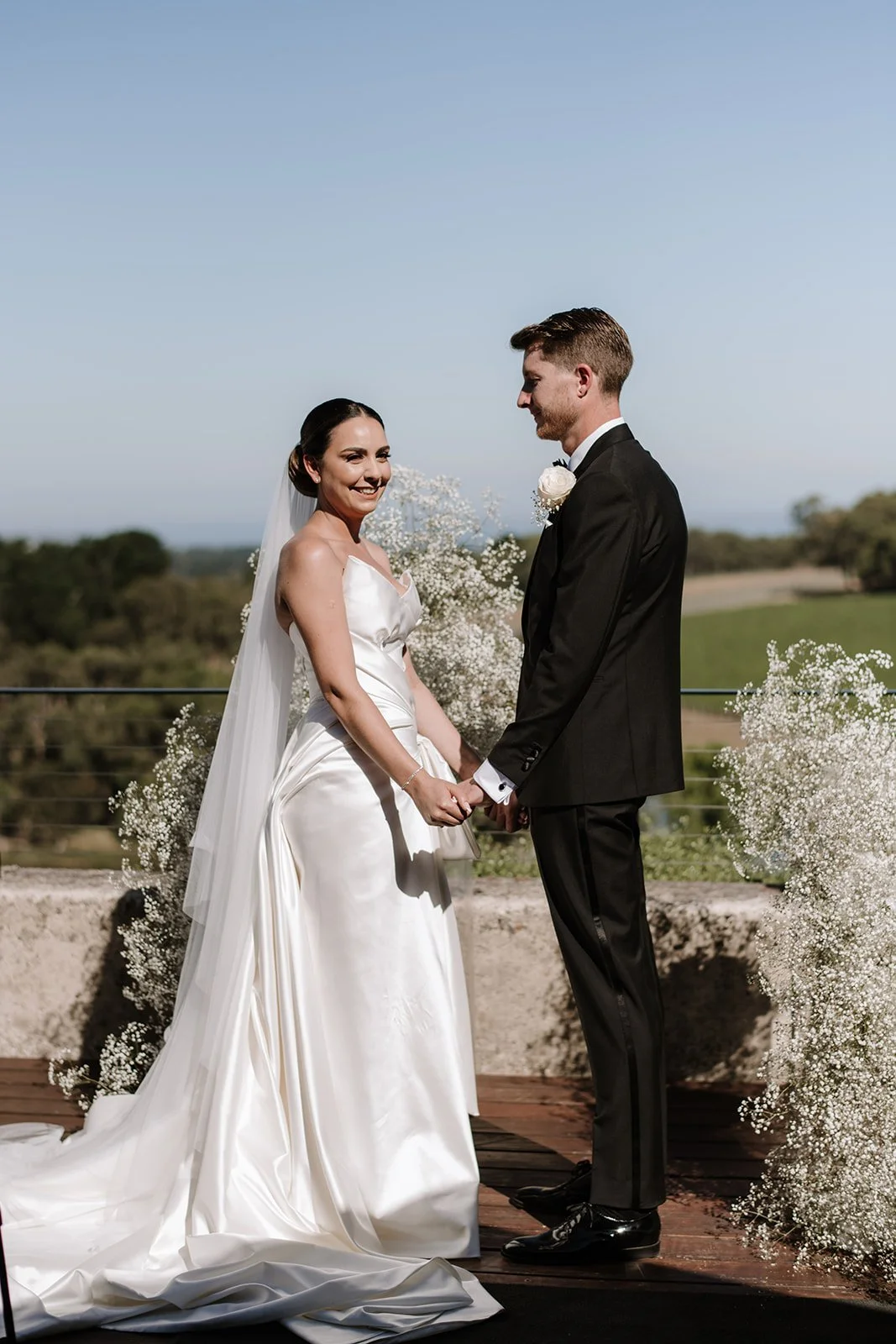 Modern outdoor wedding ceremony at Port Phillip Estate with the couple holding hands on the deck, surrounded by sculptural baby's breath arrangements styled by Poppy Culture overlooking the vineyard landscape.