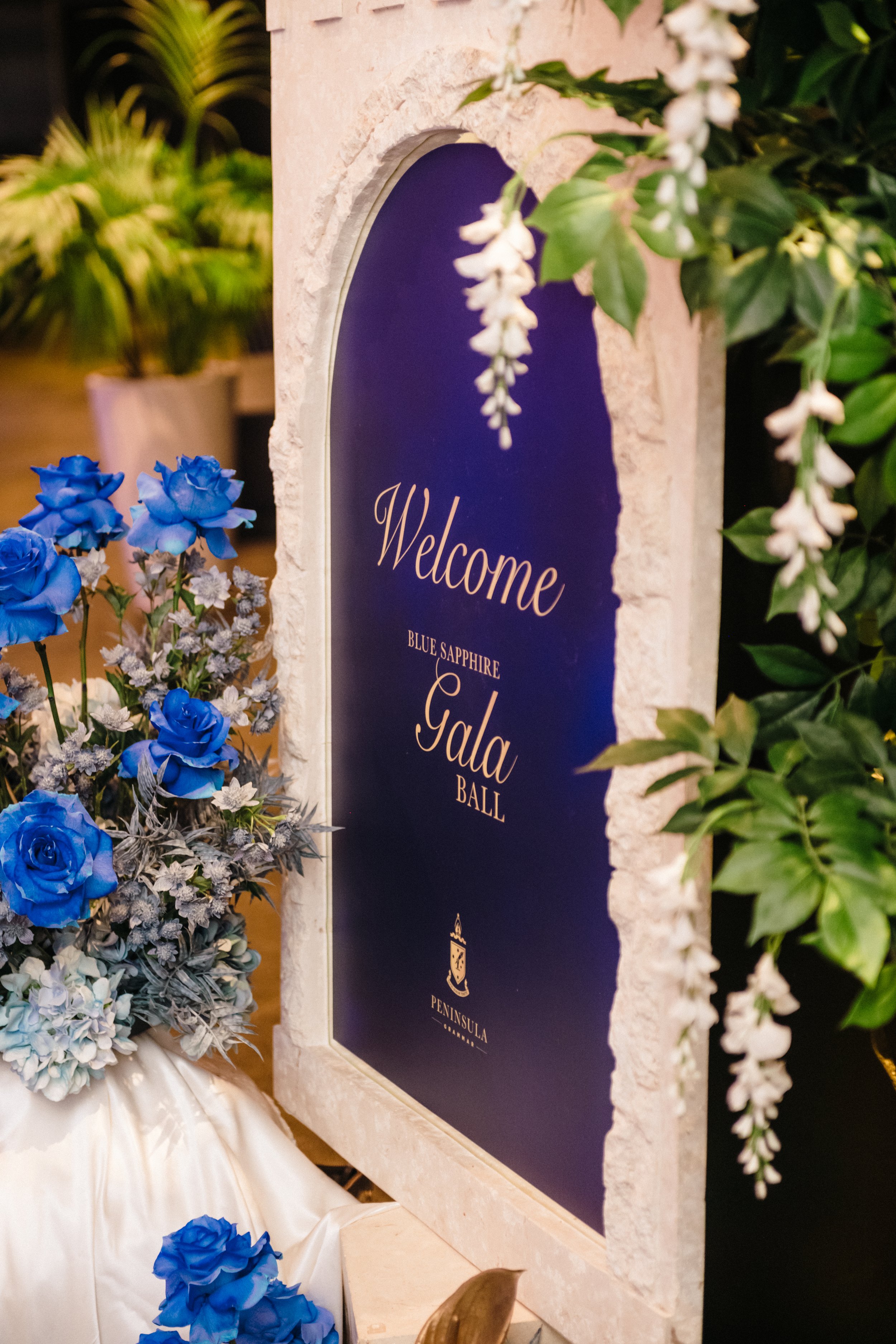 Modern‑lux corporate event styling by Poppy Culture at RACV Cape Schanck Resort, featuring a deep‑blue welcome sign framed by a white arch structure adorned with cascading white florals. Gold lettering reads “Welcome to the Annual Gala Ball,” surroun