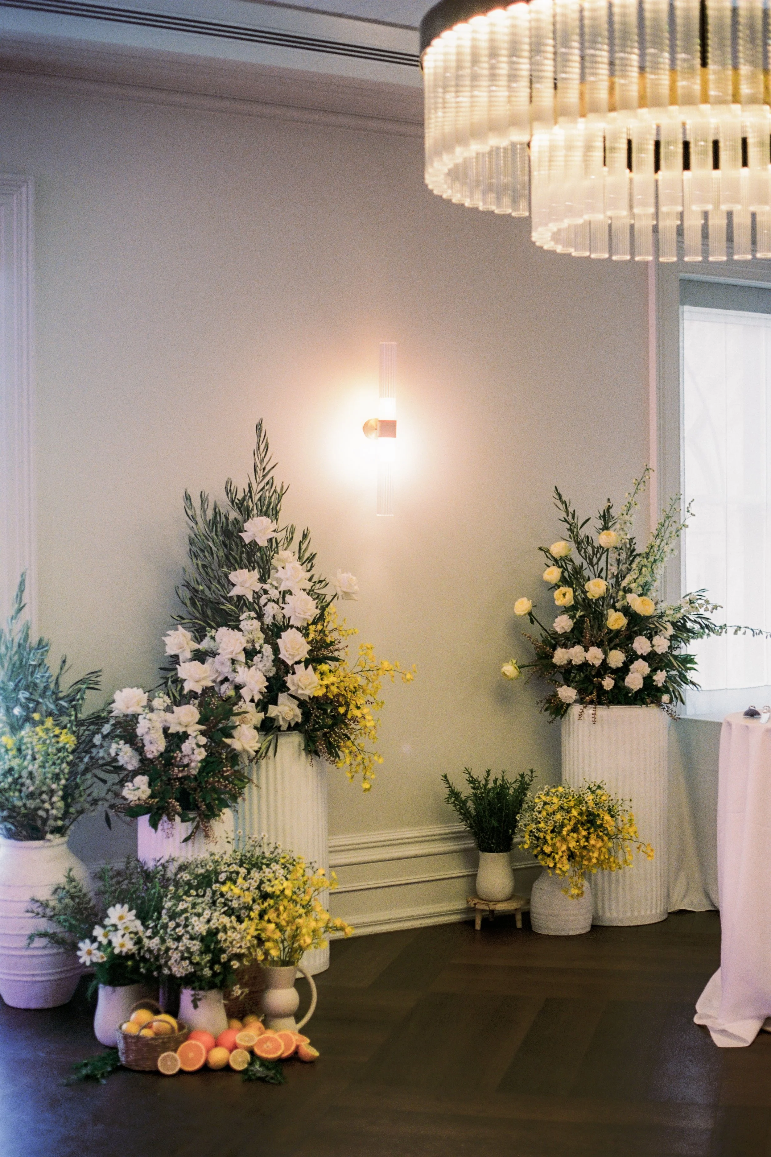 InterContinental Sorrento wedding styling by Poppy Culture with vibrant citrus accents and modern white‑and‑yellow florals arranged in layered vessels.