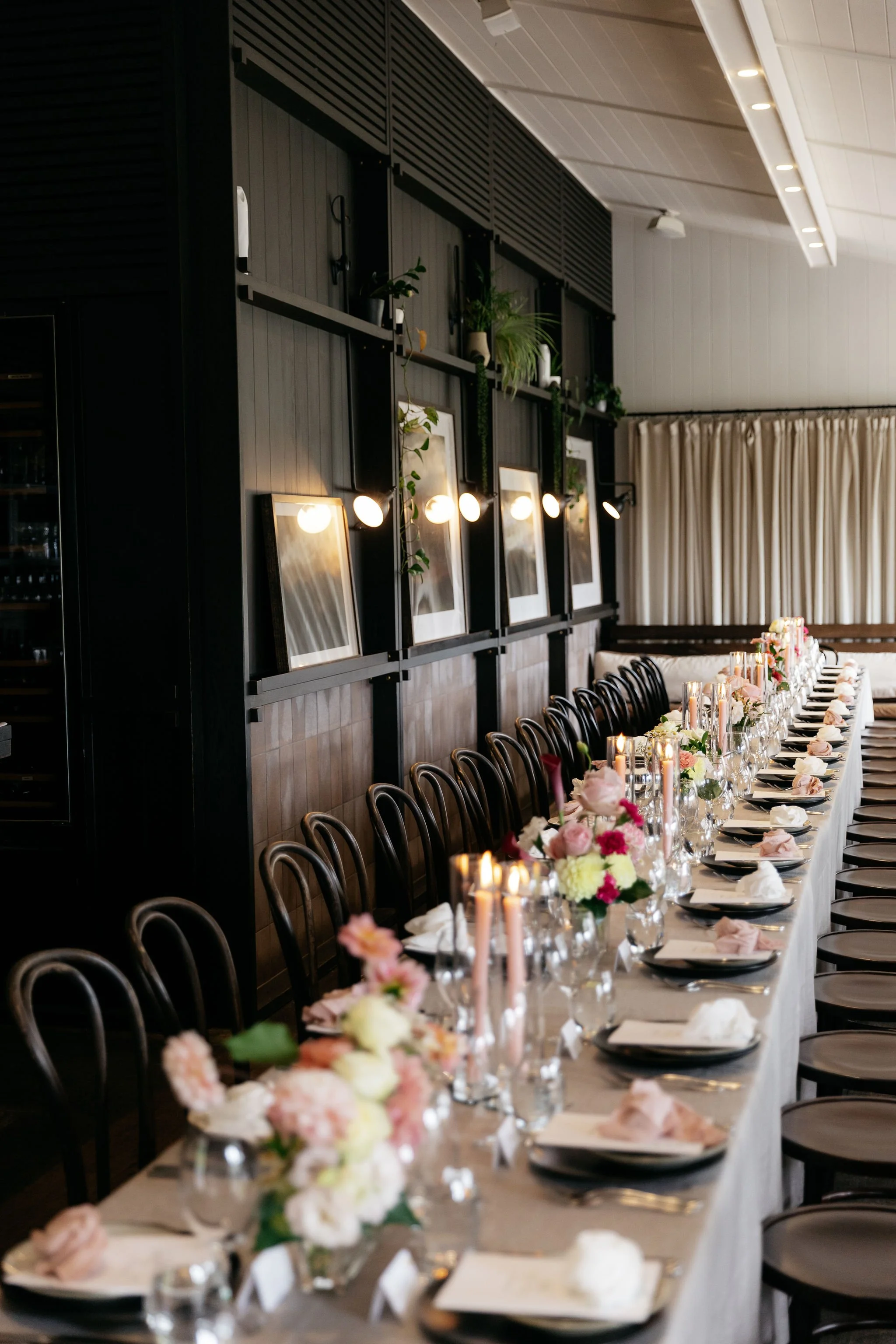 Elegant long‑table reception at Polperro with pastel floral centrepieces, pink taper candles and layered place settings styled by Poppy Culture, captured in soft natural light by Ali Bailey.