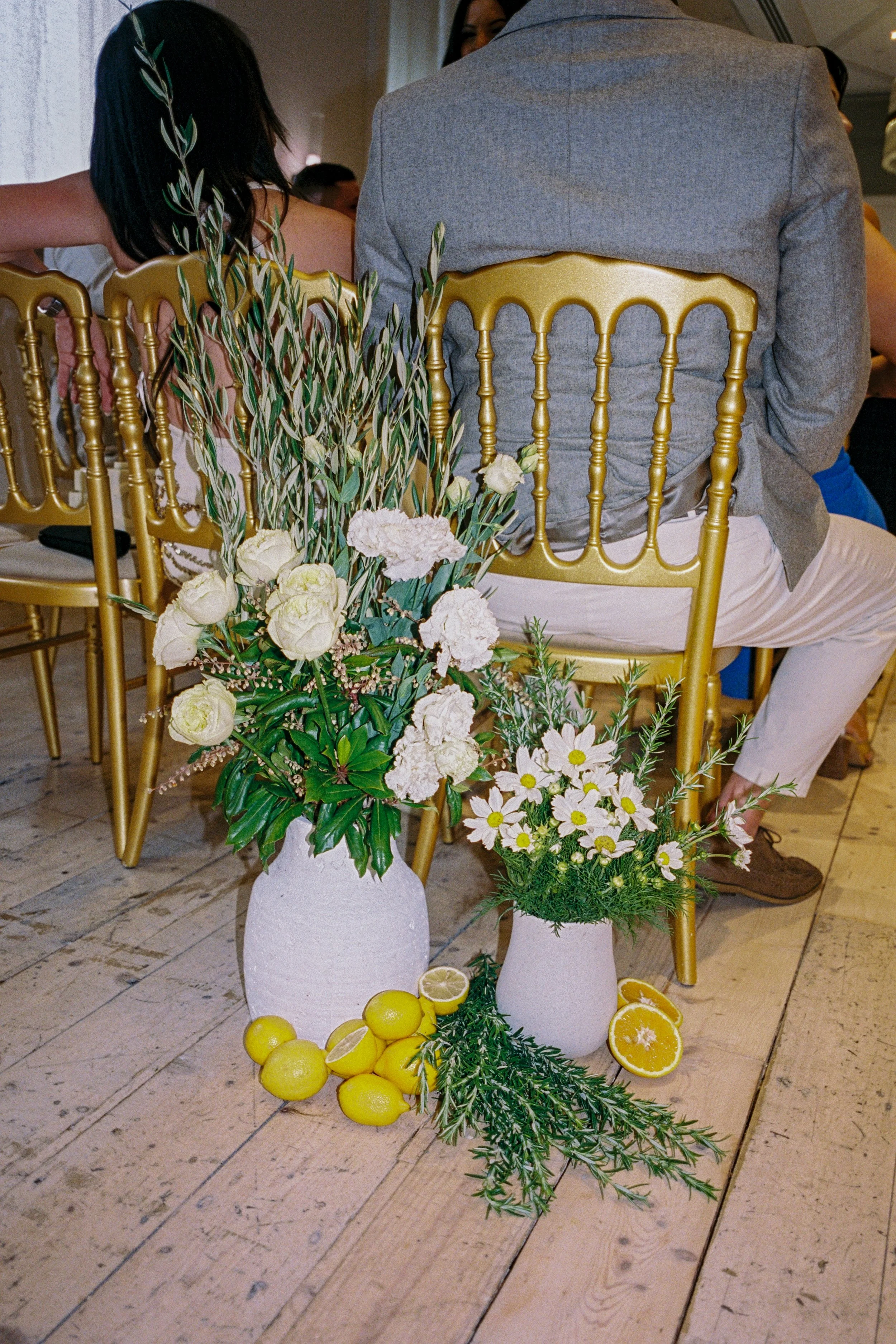 Citrus‑accented aisle arrangement at InterContinental Sorrento with Poppy Culture’s cream florals, white daisies and fresh lemons beside gold Tiffany ceremony chairs.