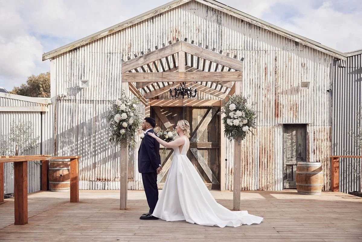 Modern wedding florals at Dromana Estate featuring white blooms and greenery framing a couple against the rustic barn façade.