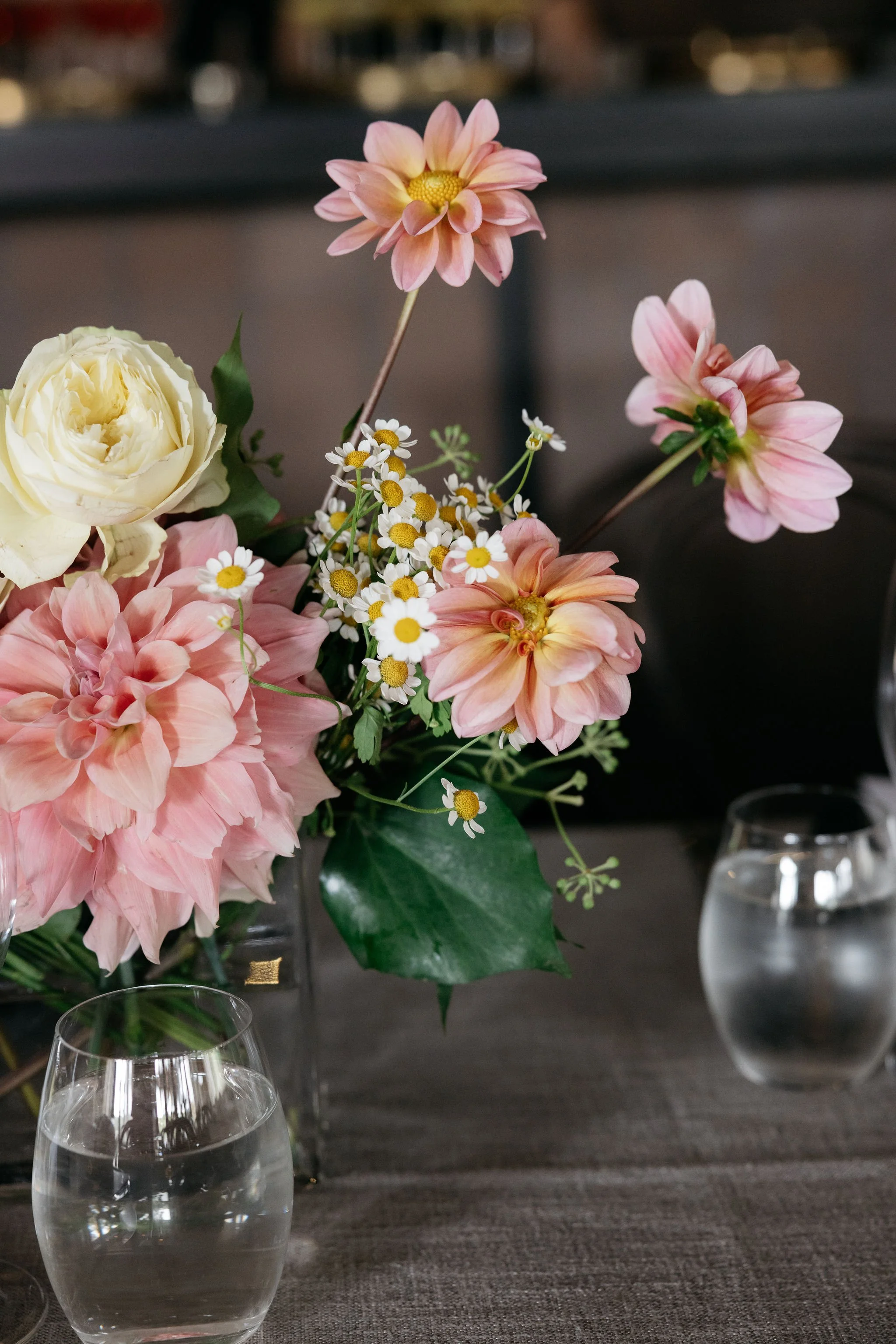 Pastel floral centerpiece at Polperro featuring pink dahlias, a cream rose and delicate daisies arranged in a glass vase, styled by Poppy Culture and captured by Ali Bailey.