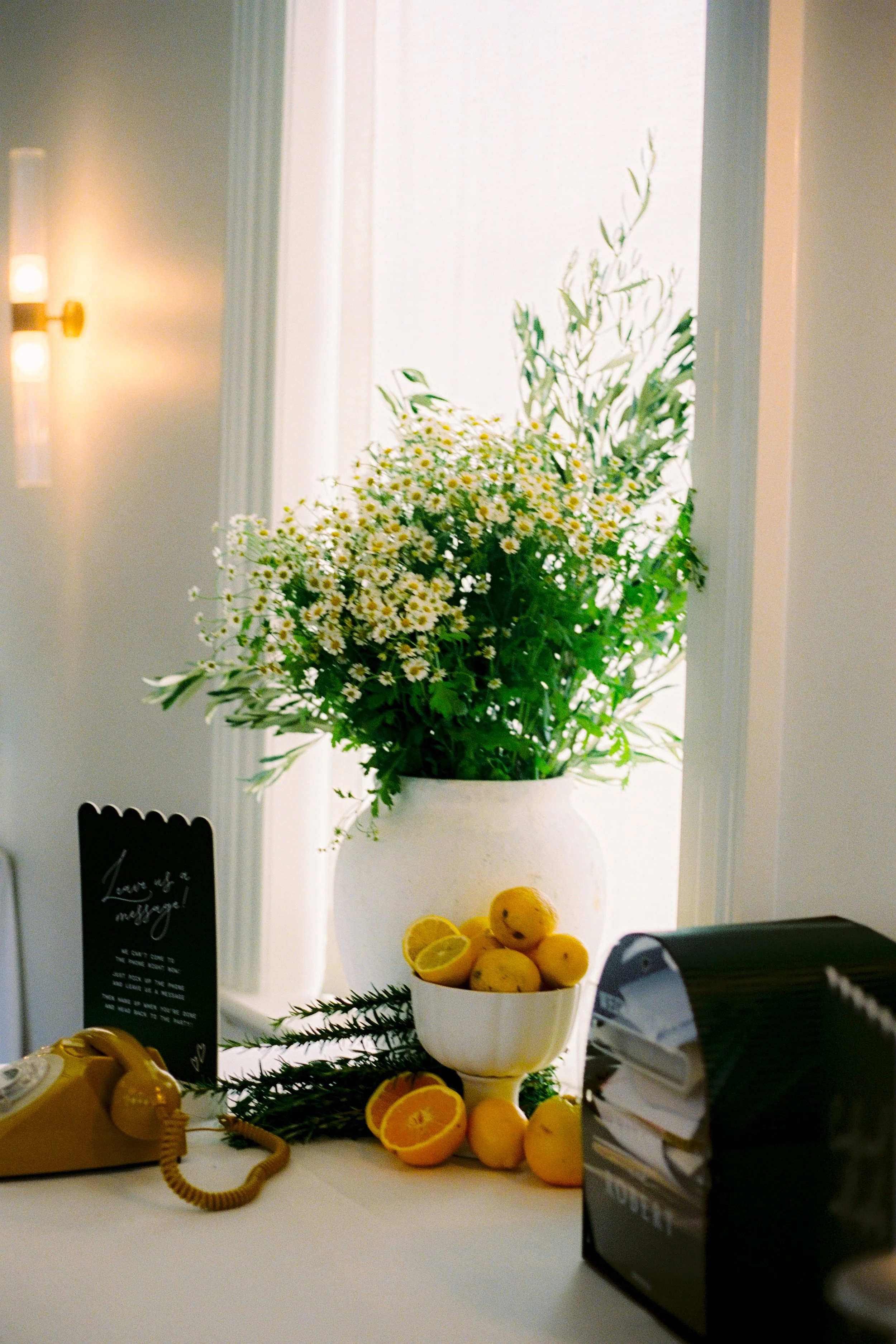 Citrus‑accented message station at an InterContinental Sorrento wedding, styled by Poppy Culture with a white floral arrangement, lemons and a vintage rotary yellow phone.