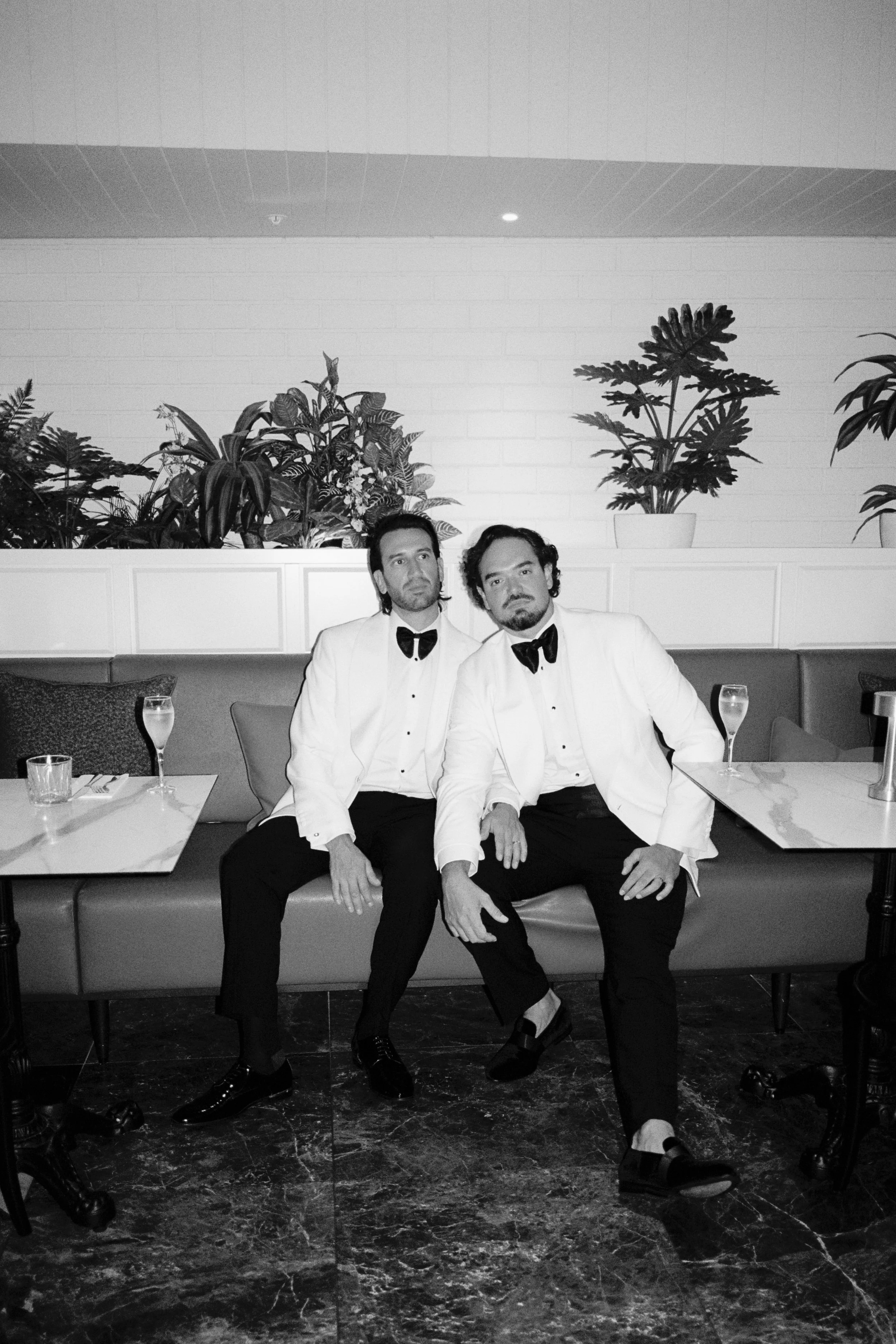 Two grooms in white tuxedo jackets seated together at InterContinental Sorrento, captured in a refined black‑and‑white editorial style.
