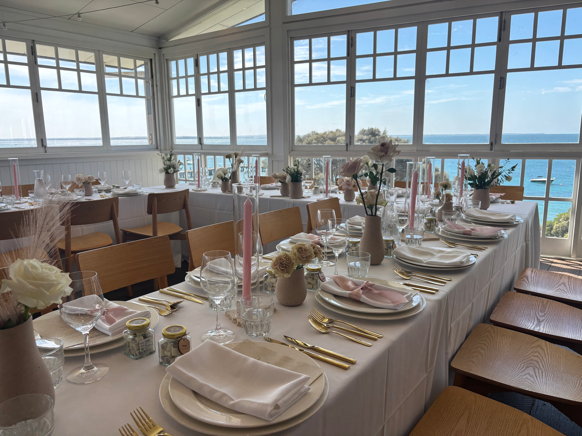Portsea Hotel coastal reception styling with soft‑toned florals, pink candles and gold cutlery set against ocean views.