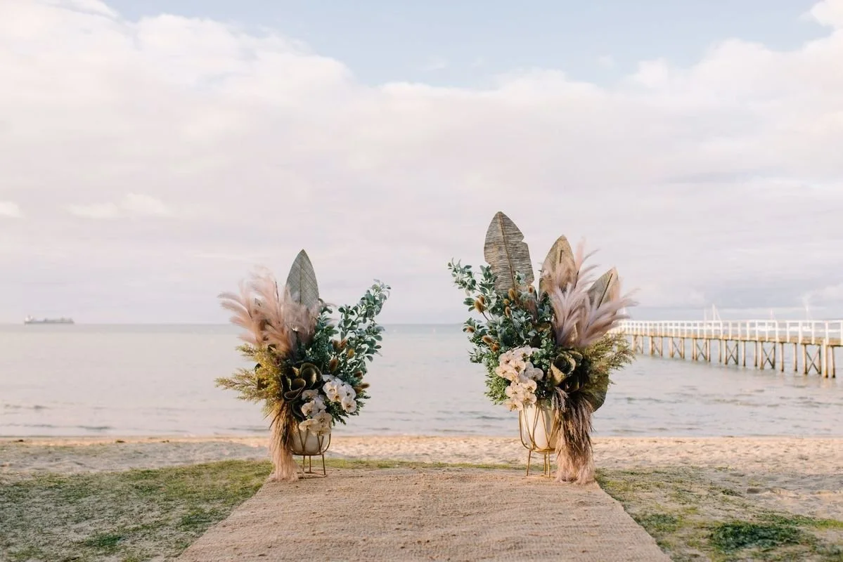 The Baths Sorrento beach ceremony with pampas and white floral arrangements framing the ocean backdrop.